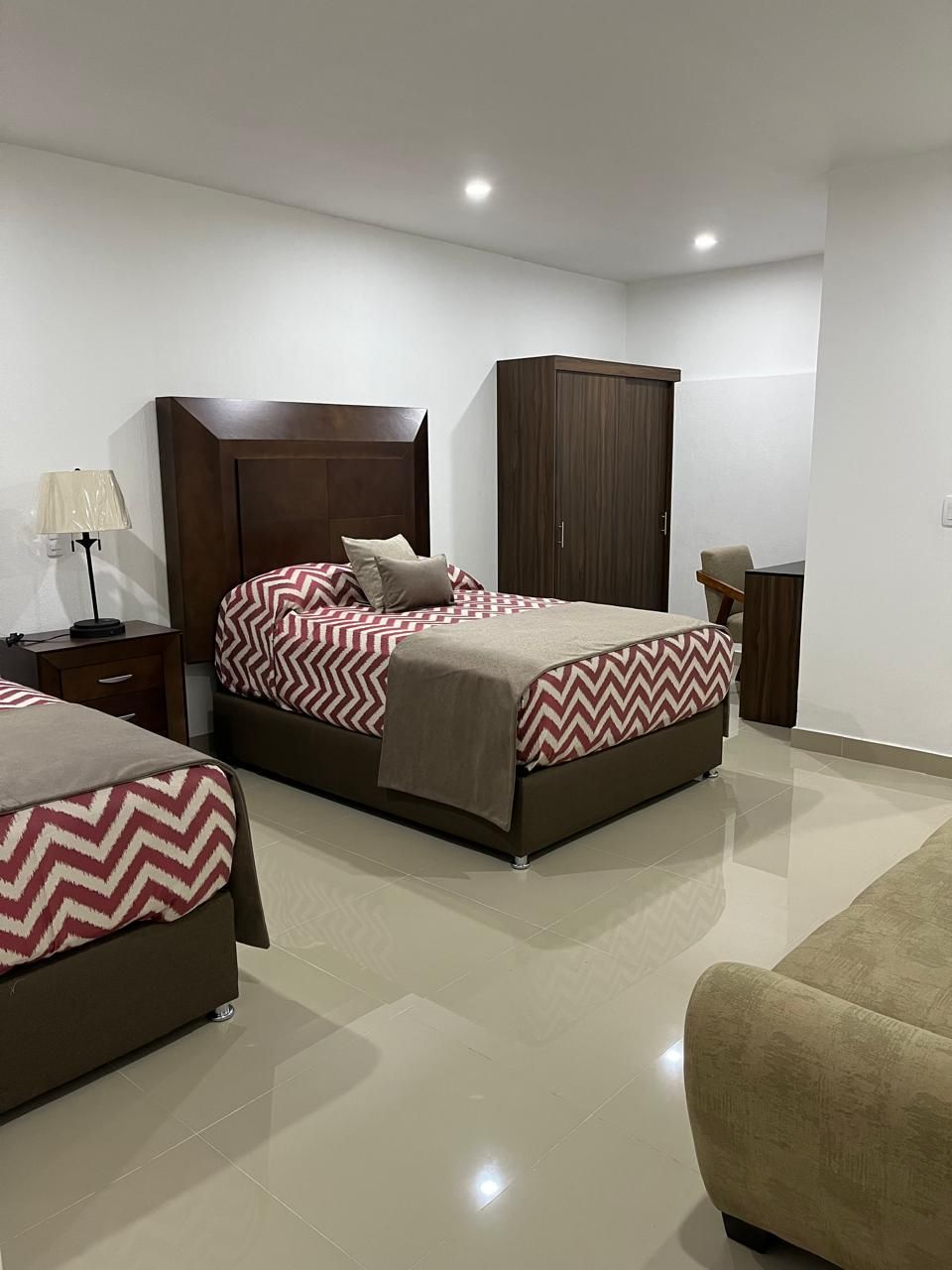 Una habitación de hotel con dos camas, un armario, un escritorio y un sofá beige.