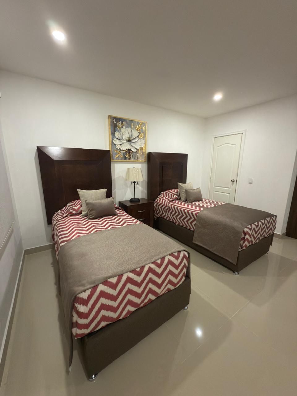 Dos camas individuales en una habitación blanca con cabeceras marrones, ropa de cama con estampado de chevrones 