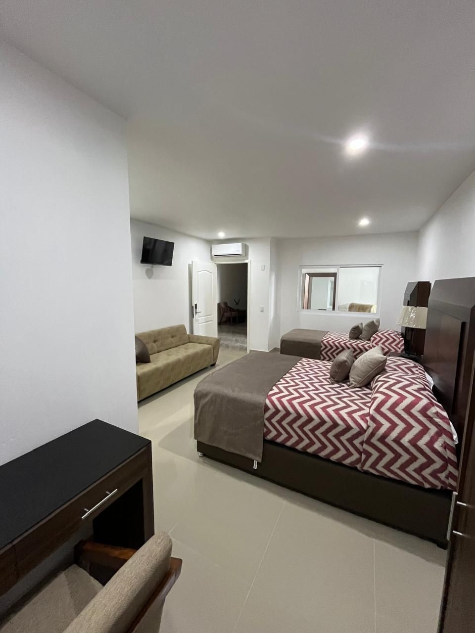 Habitación de hotel con dos camas, sofá, escritorio y puerta abierta a otra habitación.