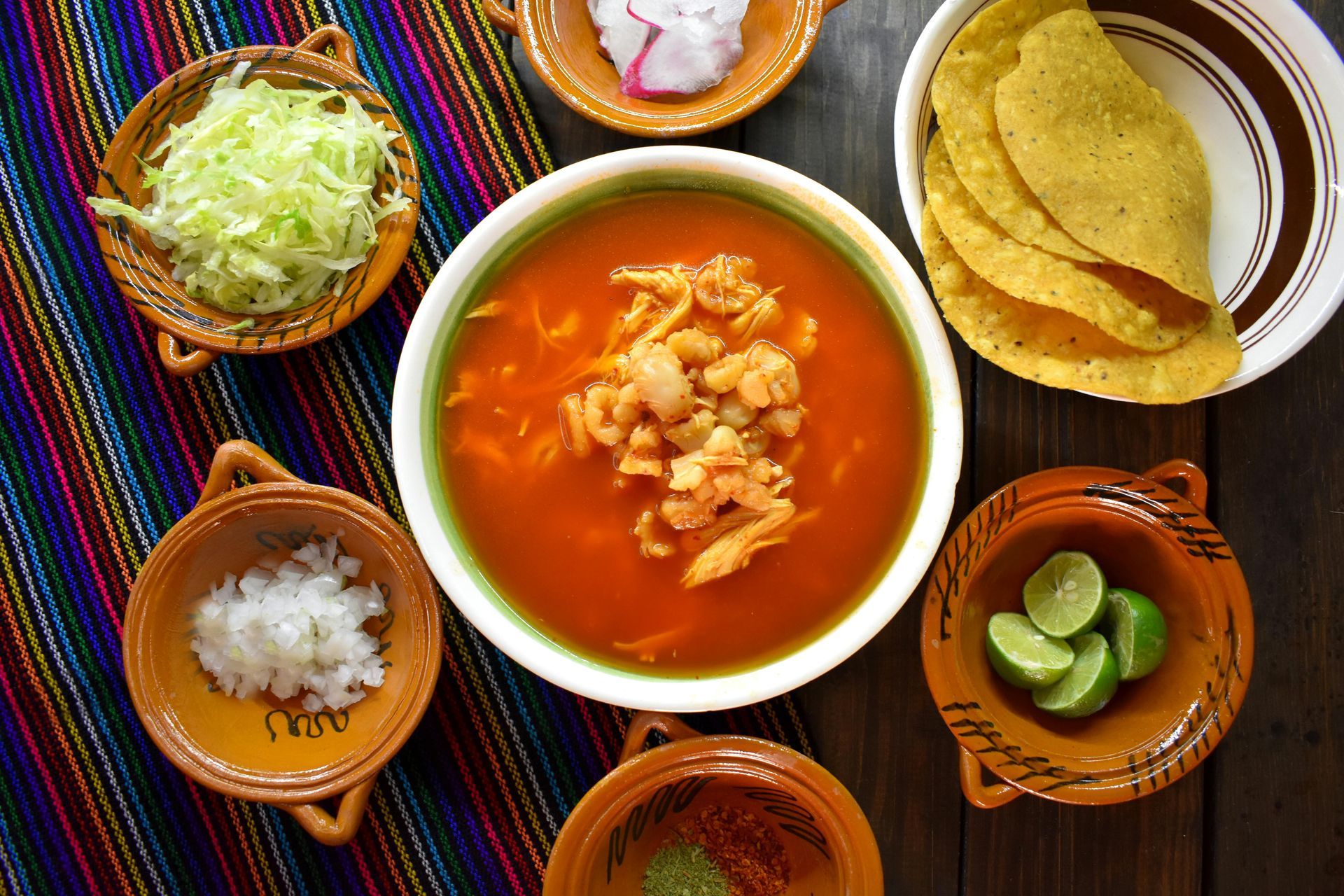 Sopa de pozole con aderezos de lechuga, rábano, cebolla, limón y tortillas.