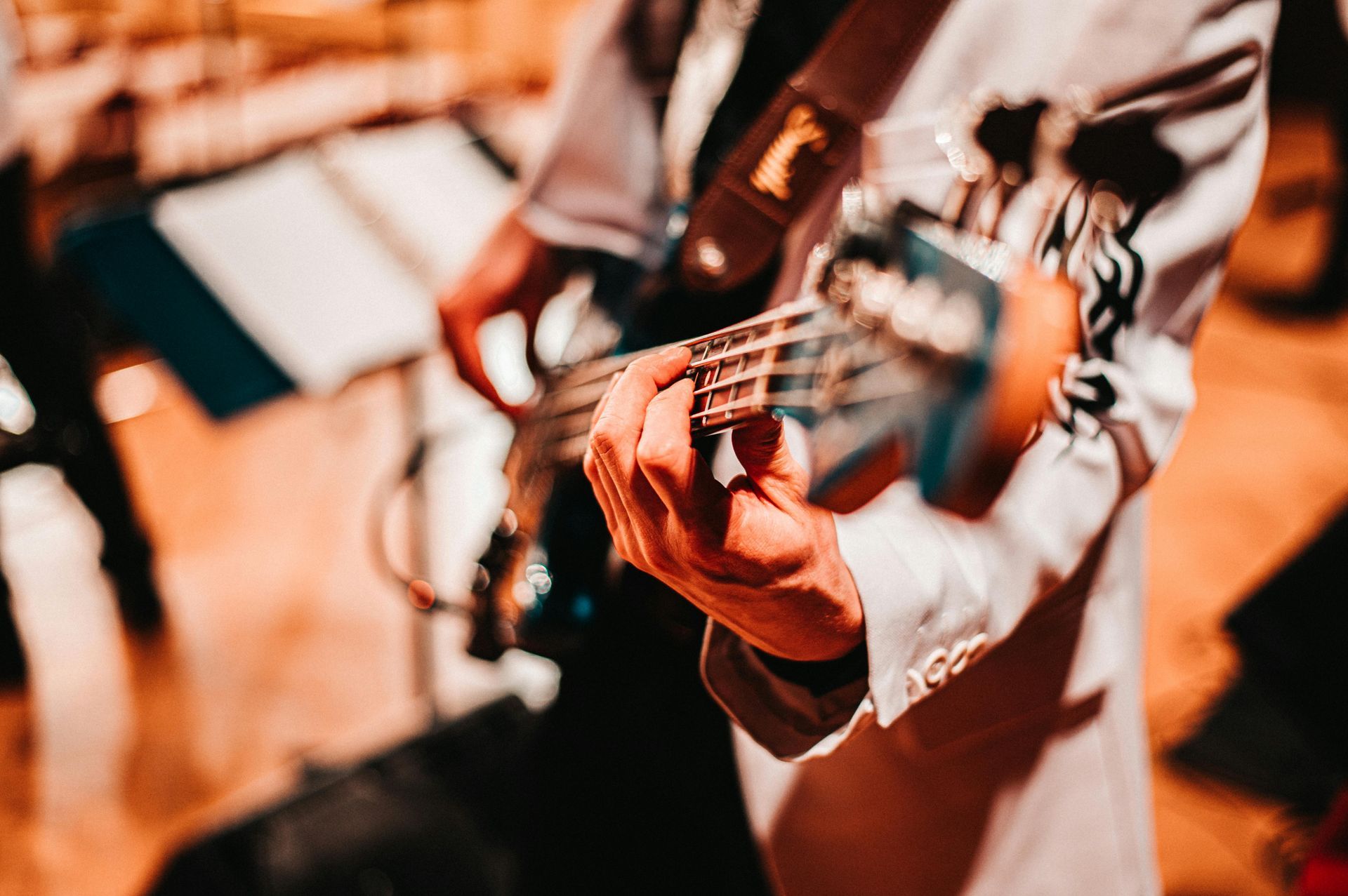 Persona con traje blanco tocando un bajo; vista de cerca de las manos en el diapasón, configuración de la banda.