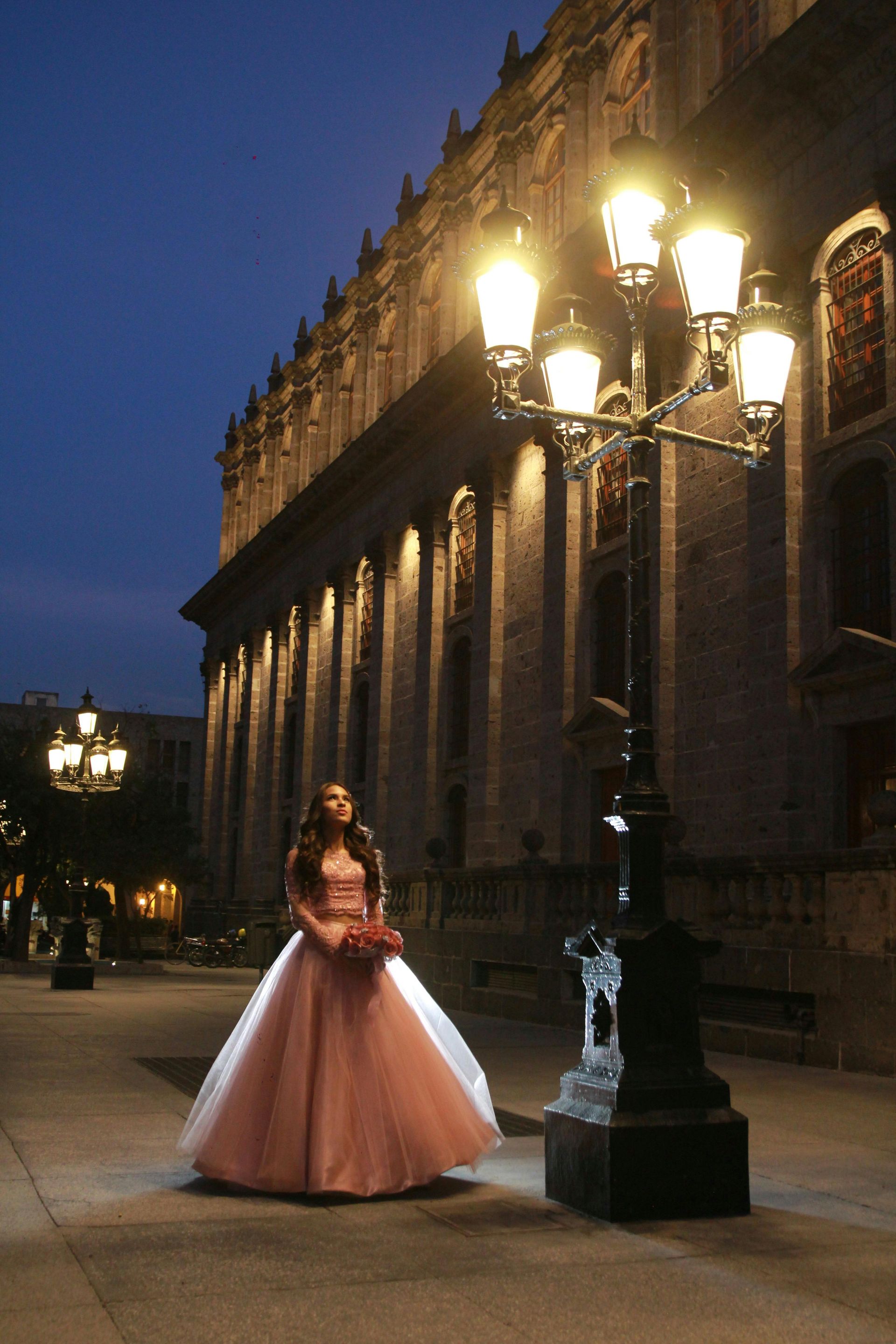 Una mujer con un vestido rosa está parada cerca de un poste de luz adornado
