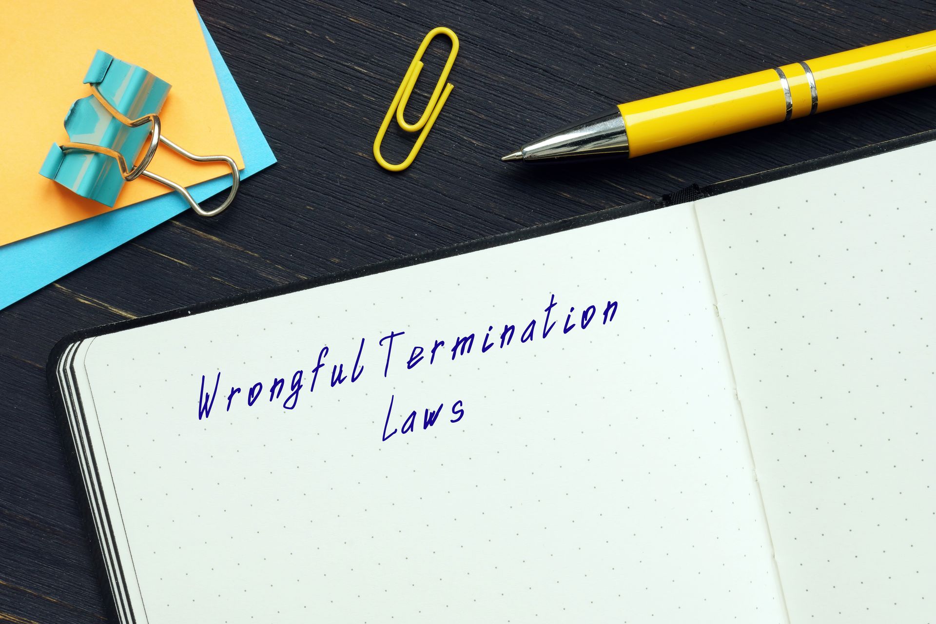 Notebook displaying the words “Wrongful Termination Laws” beside office supplies on a desk.