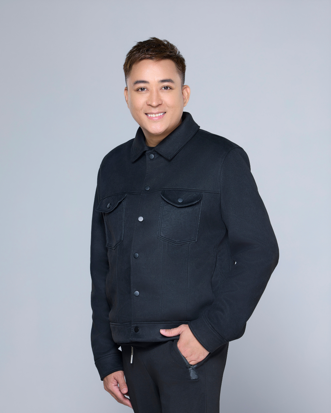 Man in black jacket, smiling, posing against a gray backdrop.