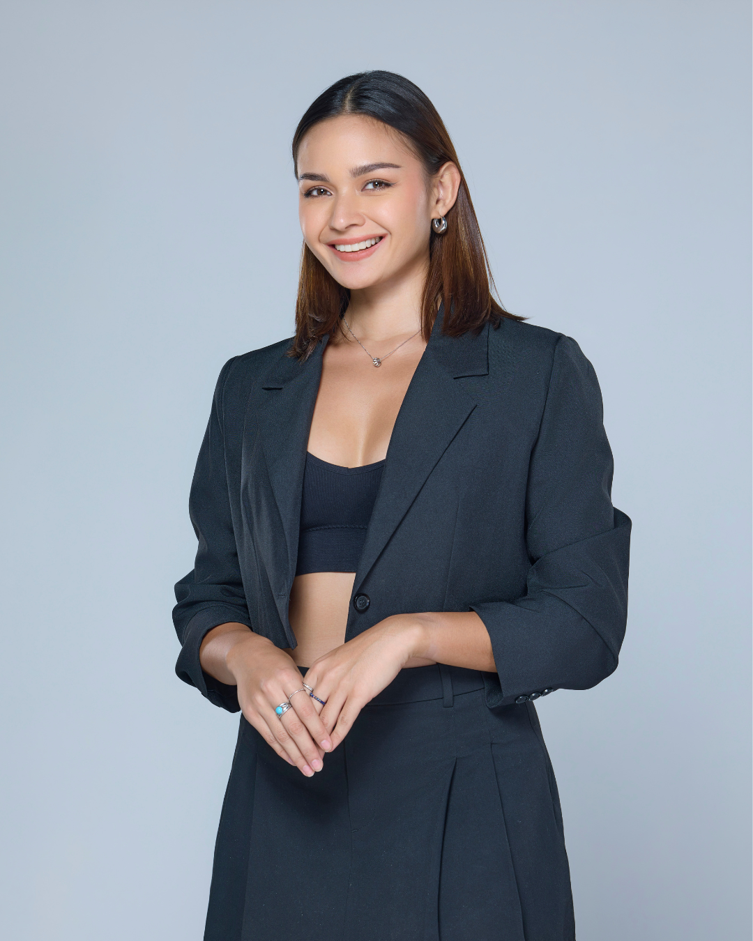 Woman in a dark suit, smiling. She wears a black top and has dark hair.