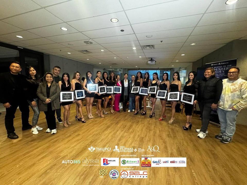 Group poses with framed awards in a room. Many women in black dresses stand alongside men.