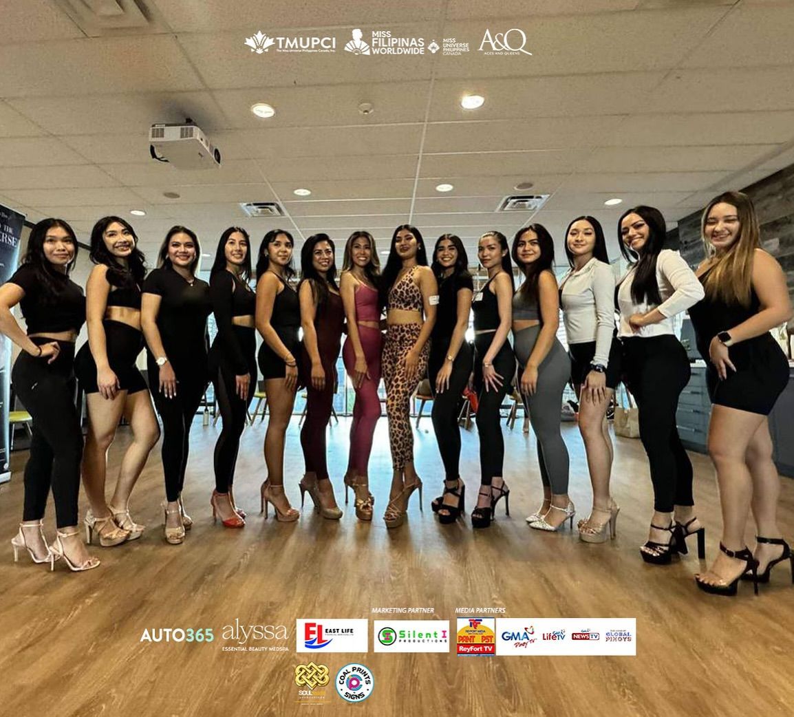 Group of women in heels pose for a photo in a room, some wearing black outfits.