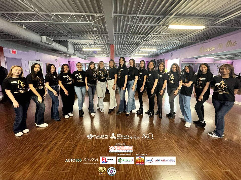 Group of women in a dance studio, wearing black shirts and jeans, smiling at the camera.