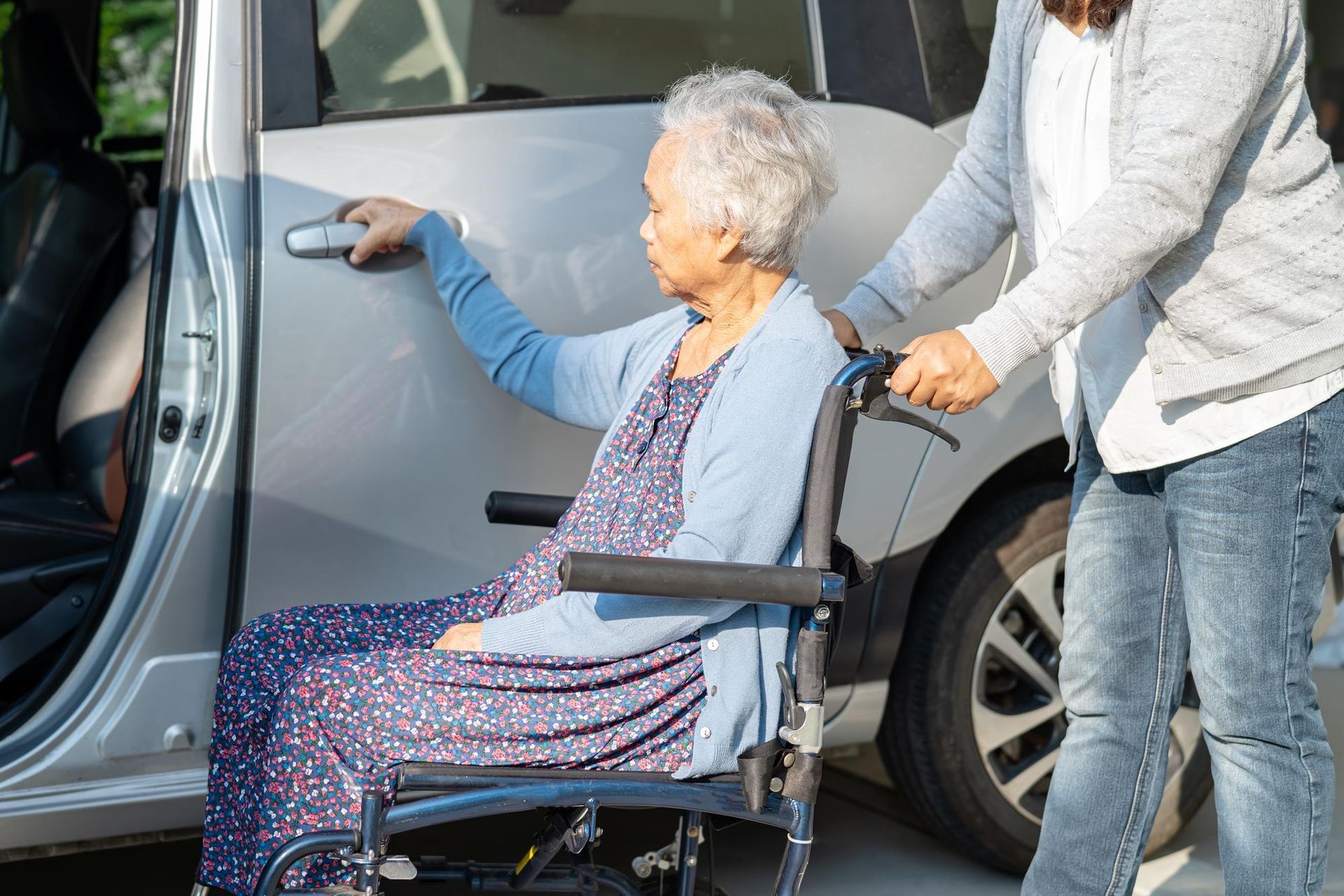 An elderly woman in a wheelchair is getting out of a car.