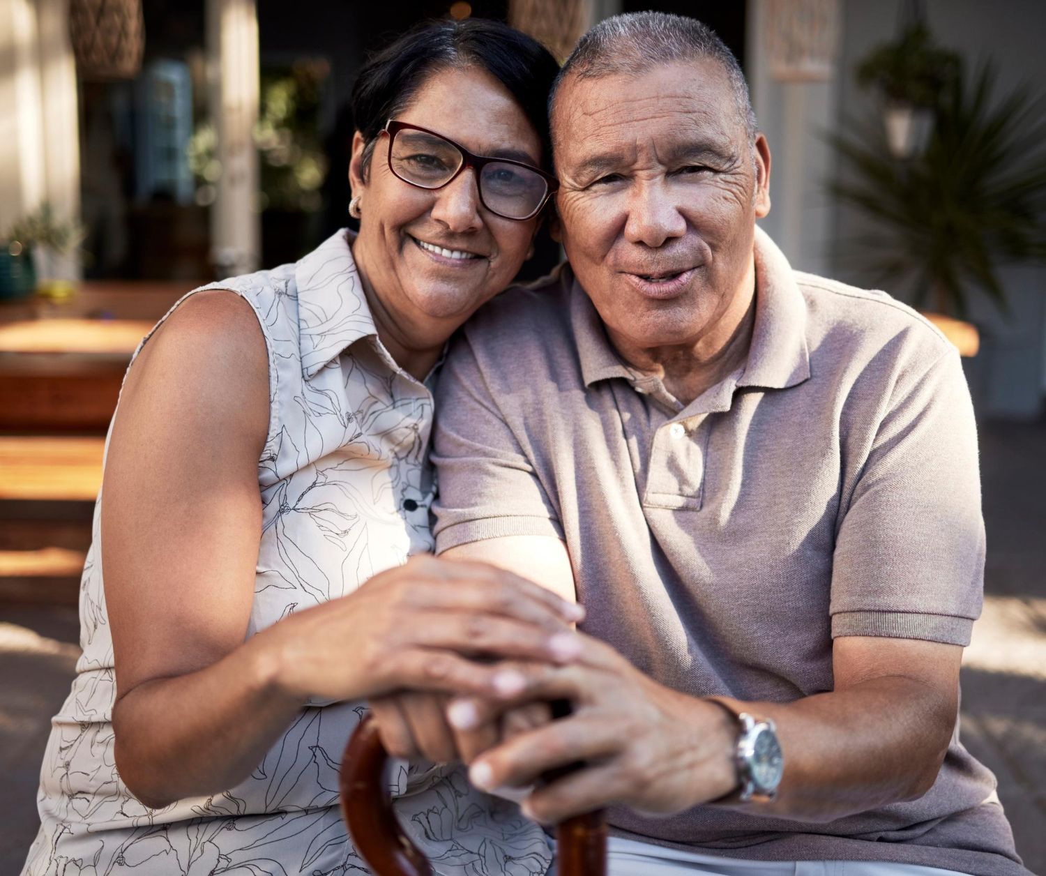 A man and a woman are sitting next to each other on a bench . the woman is holding a cane.