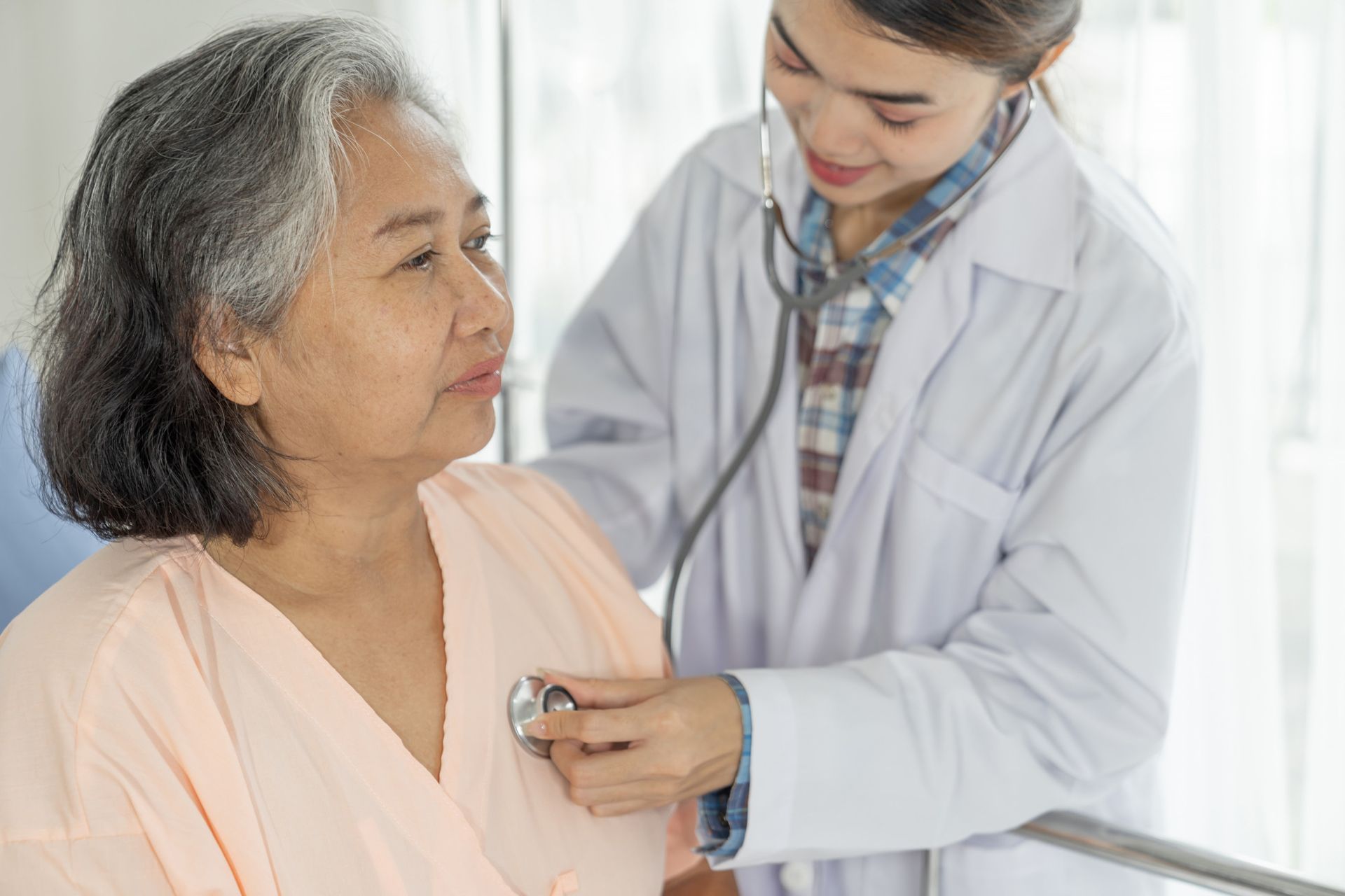 A doctor is listening to an elderly woman 's heart with a stethoscope.