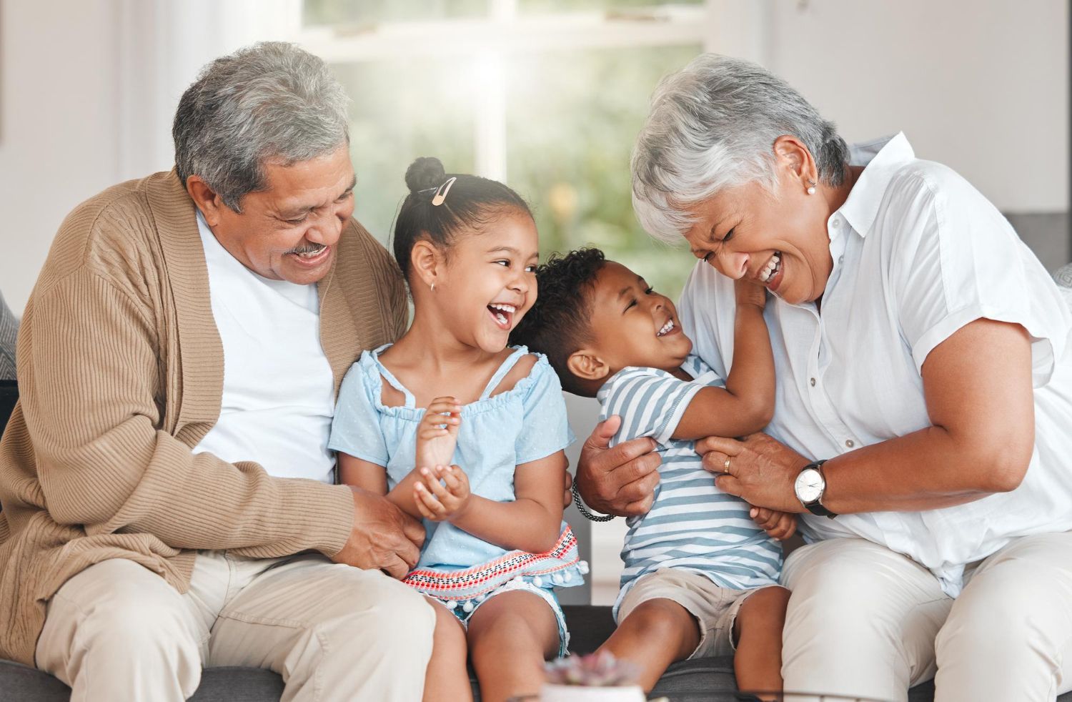 A family is sitting on a couch playing with their grandchildren.