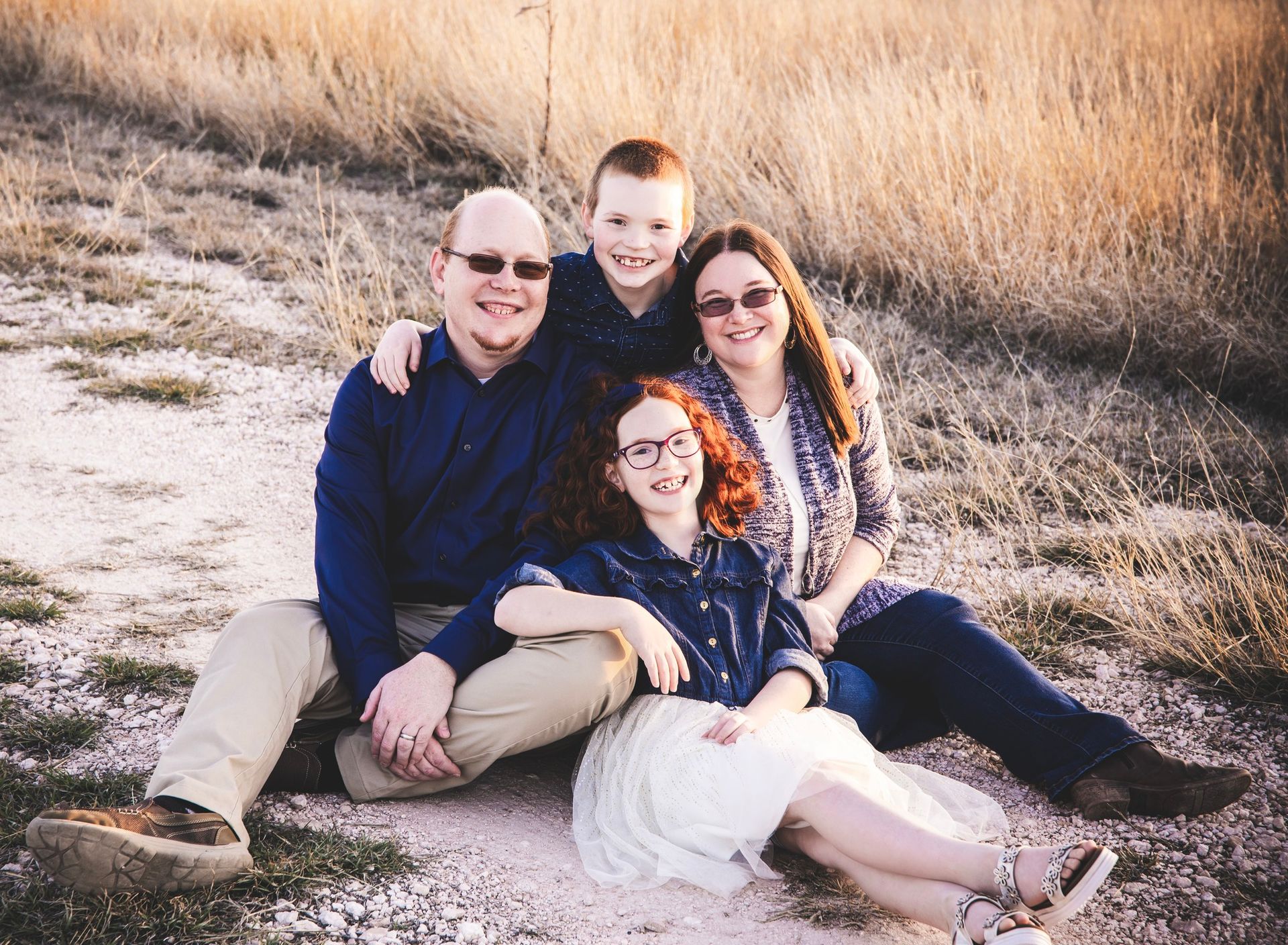 A family is posing for a picture while sitting on the ground in a field.