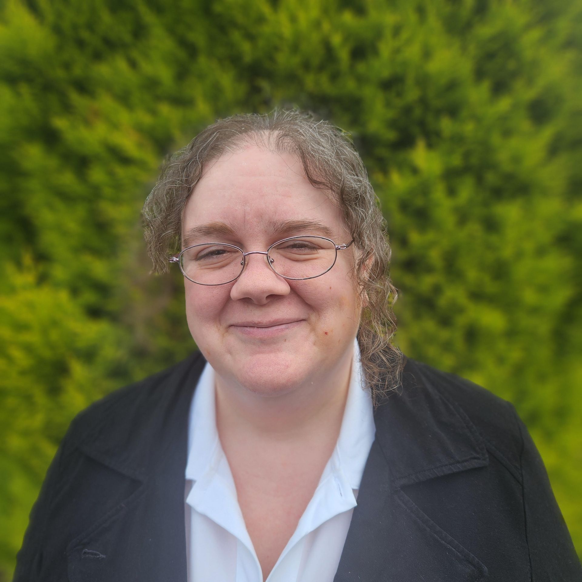 A woman wearing glasses and a black jacket is smiling for the camera.