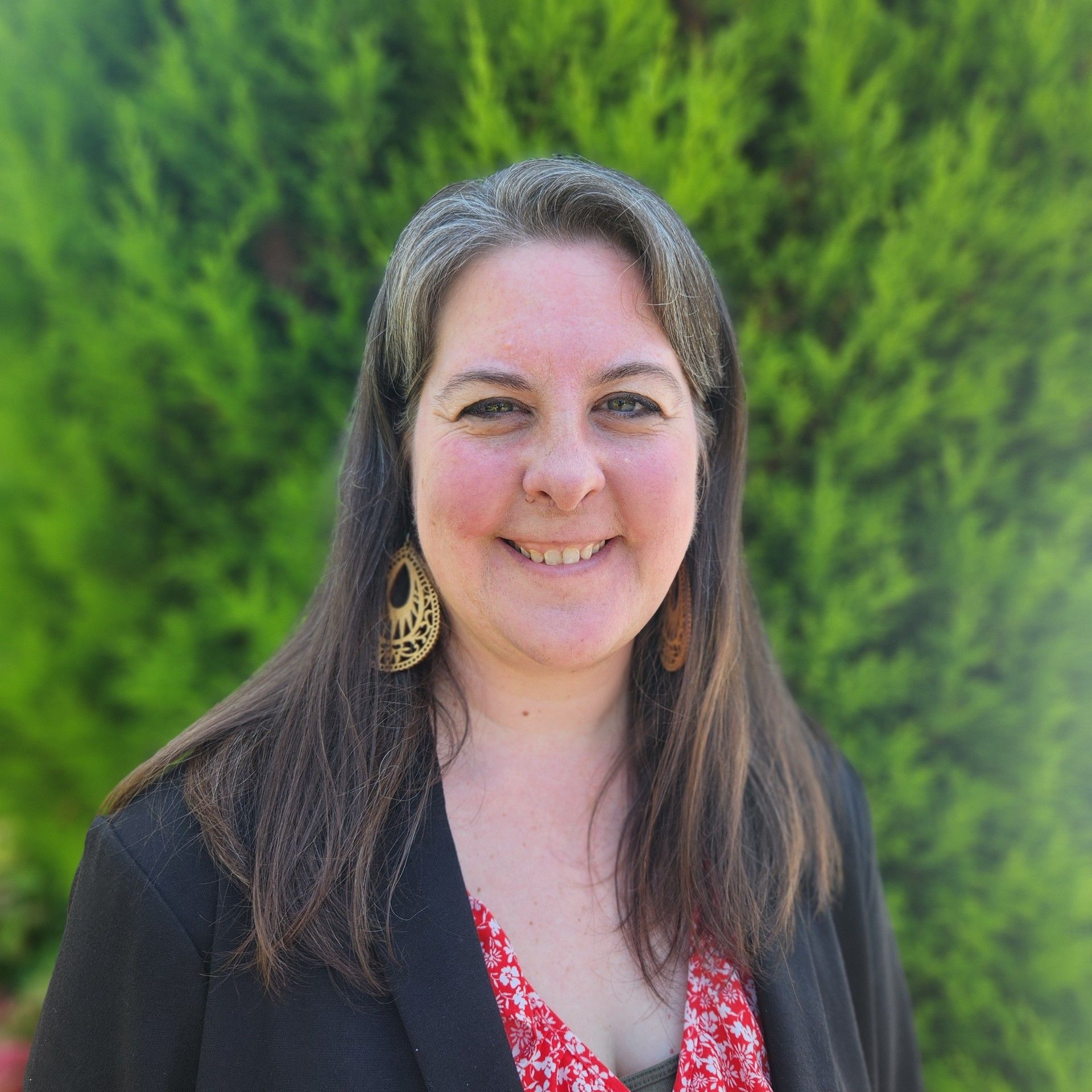 A woman wearing a black jacket and earrings is smiling for the camera.