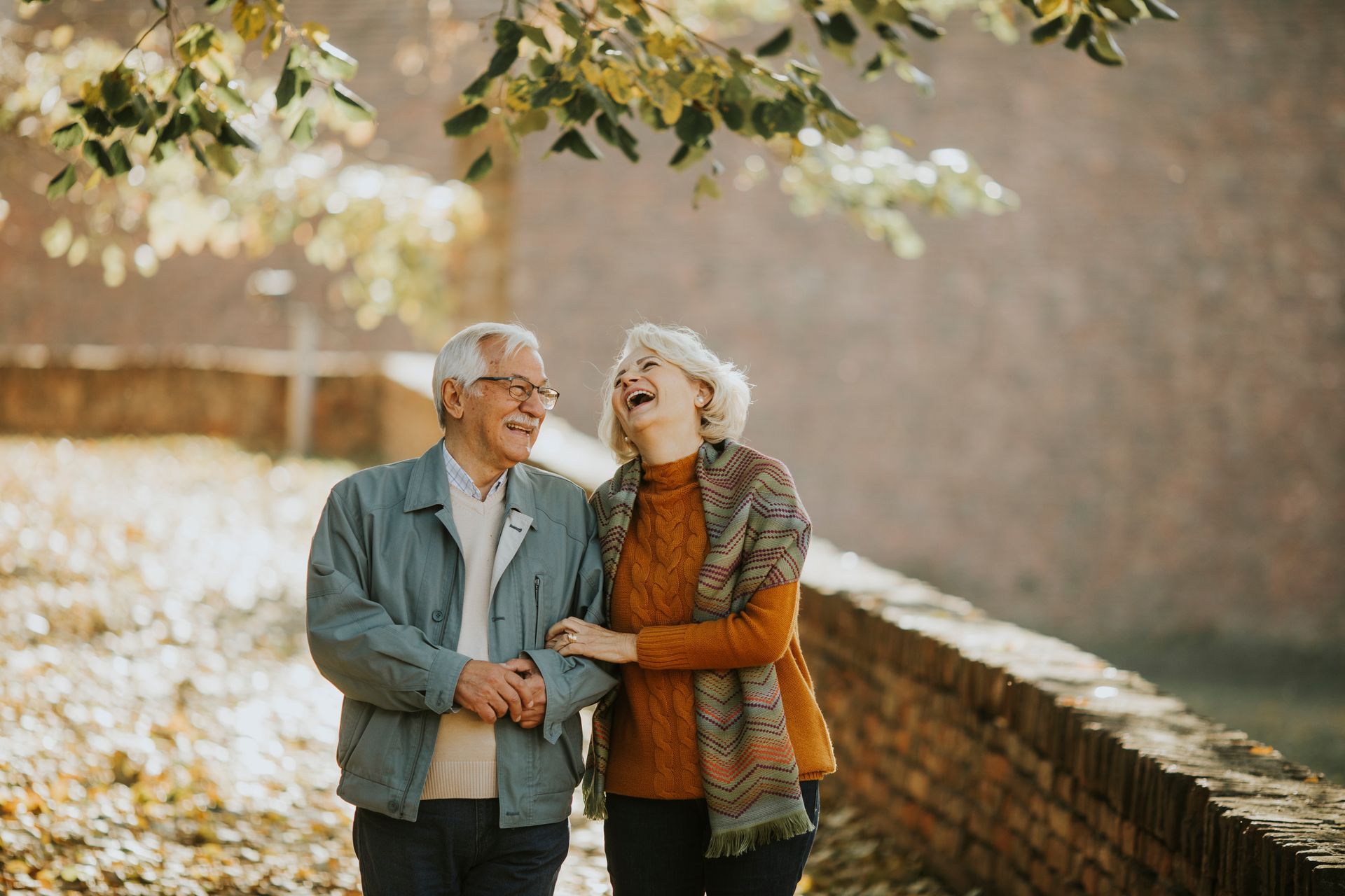 An elderly couple is laughing while walking in a park.