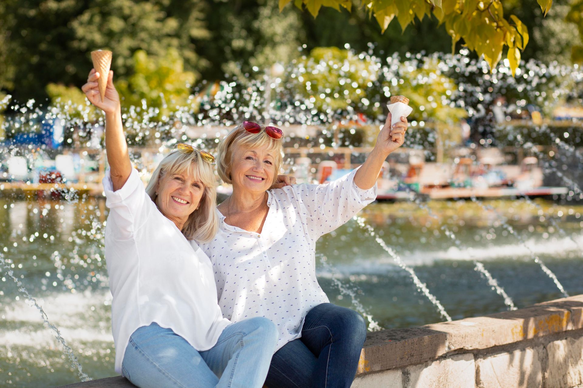 Two older women are sitting next to each other holding ice cream cones in front of a fountain.