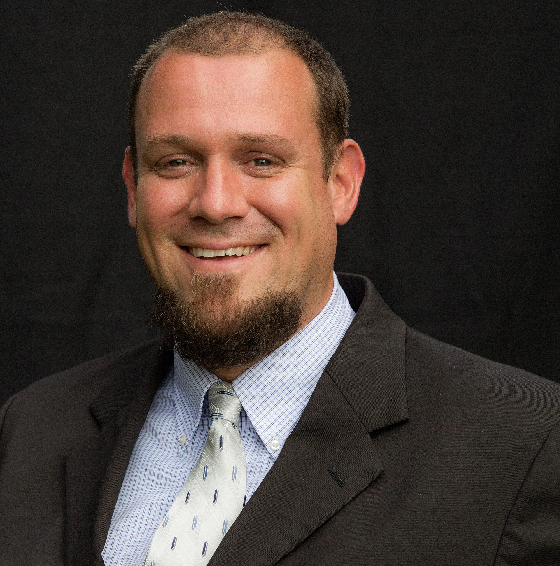 A man with a beard is wearing a suit and tie and smiling.