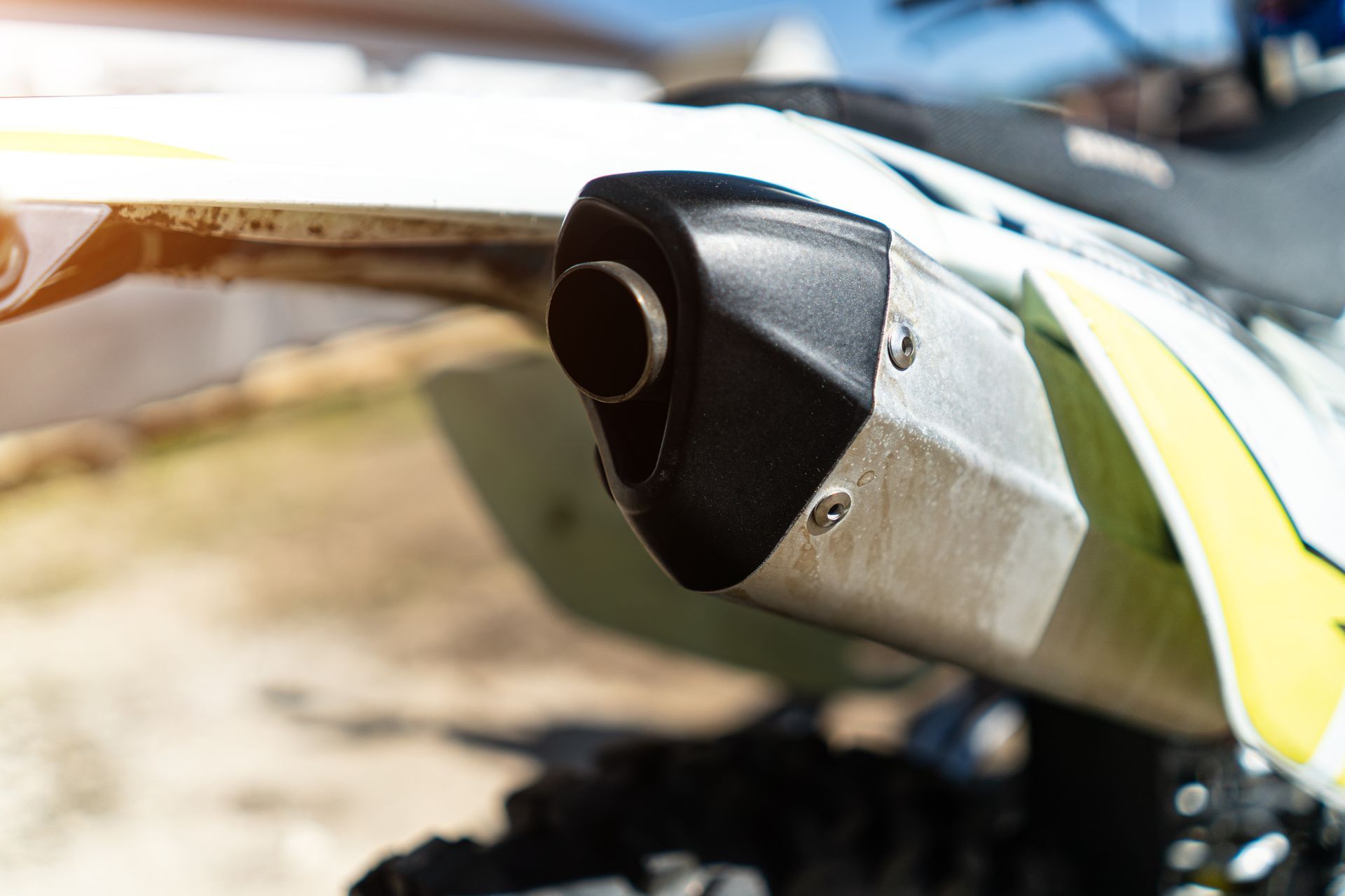 A close up of a motorcycle exhaust pipe on a dirt road.