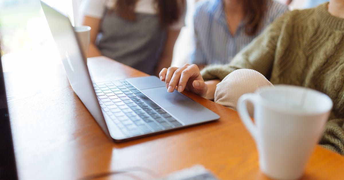 Two women are sitting at a table using a laptop computer.