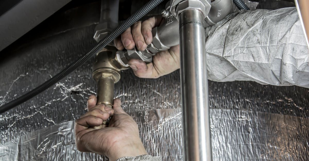 A plumber is fixing a pipe under a sink with a wrench.