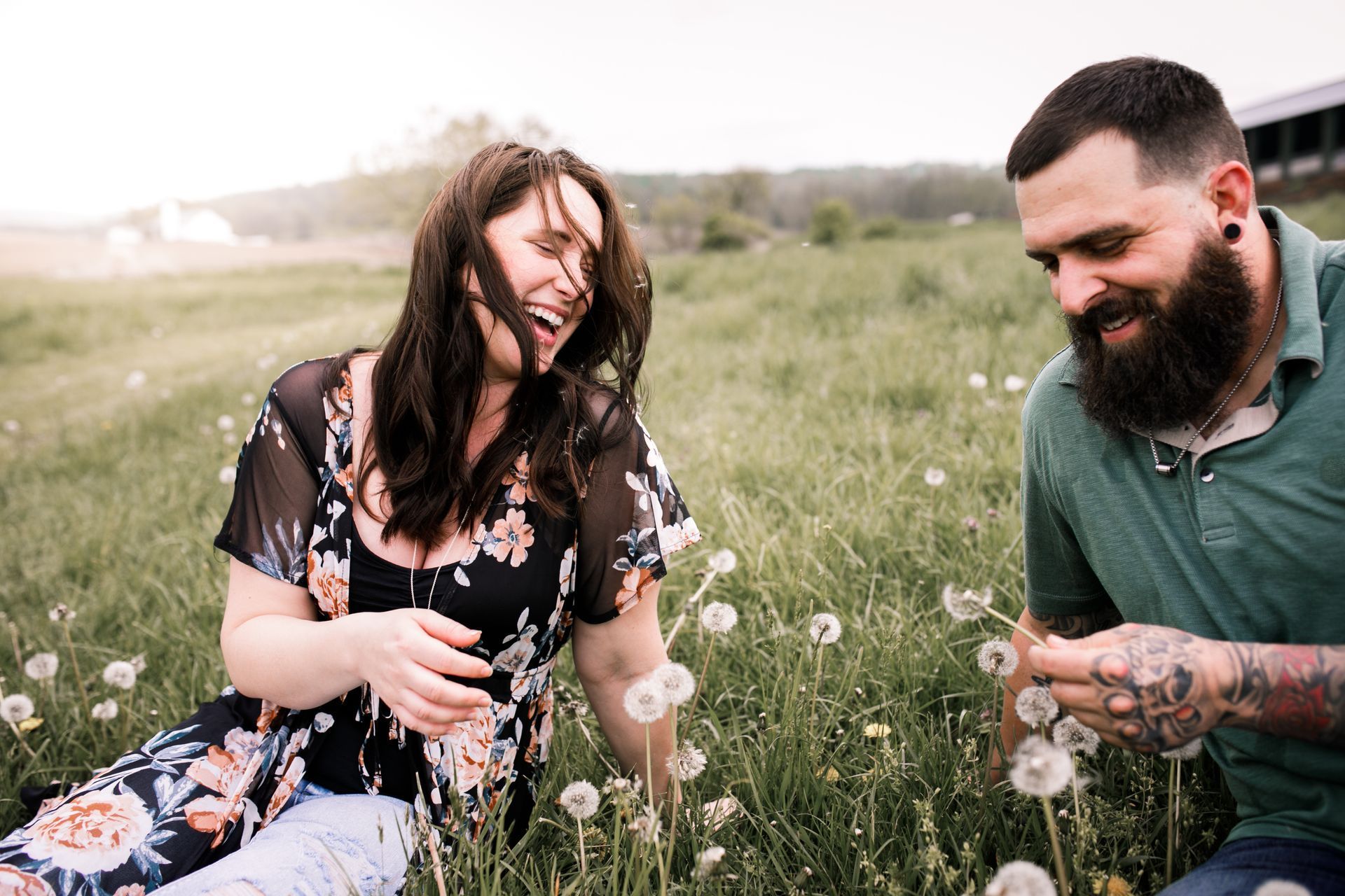 Woman laughing, man smiling, picking dandelions in a field of grass.