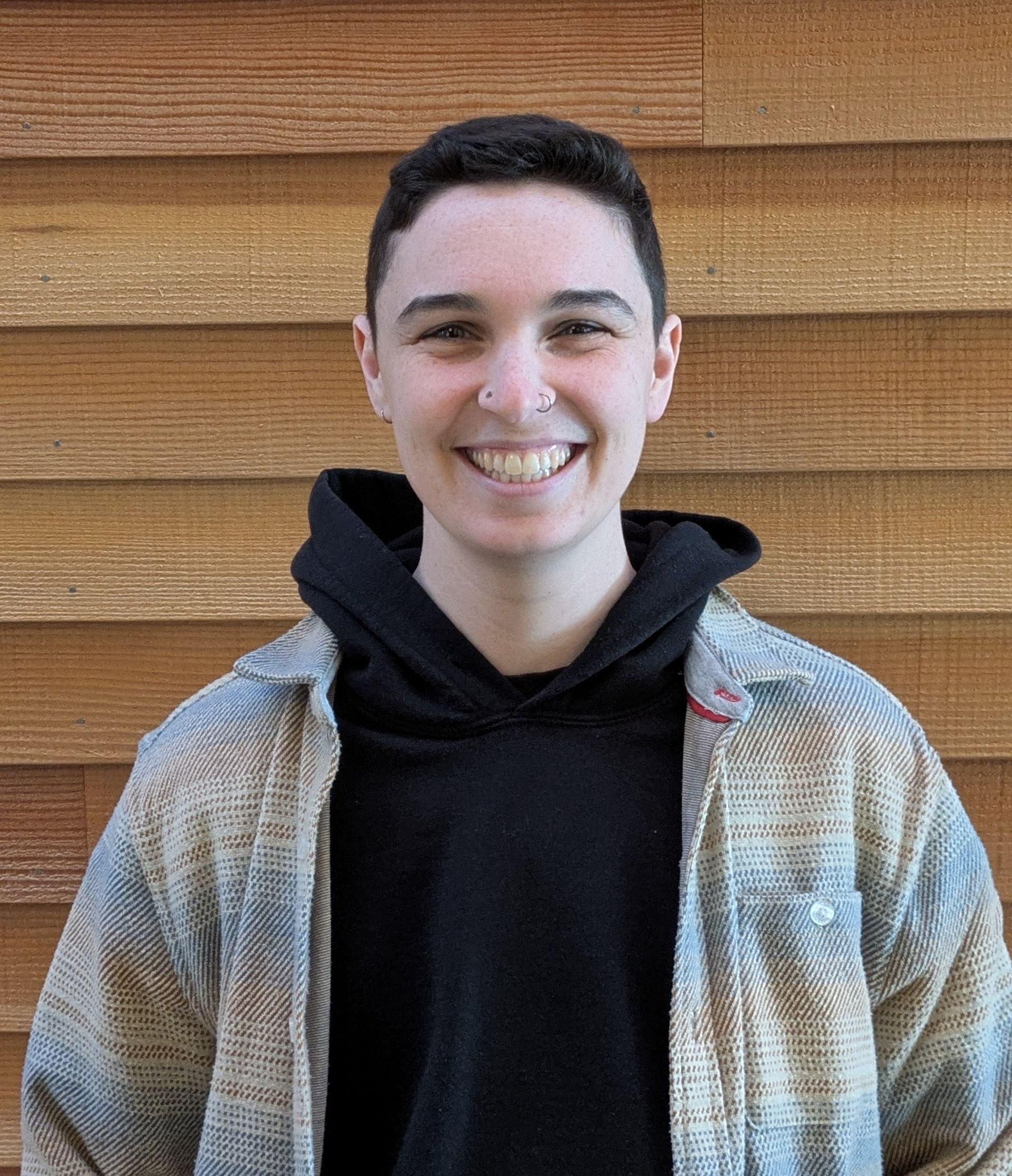 Woman with glasses smiles, wearing a light blue sweater, in front of a wood-paneled wall.