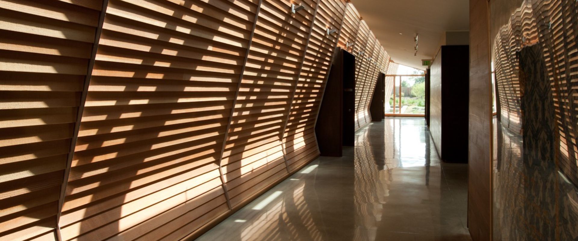 Long hallway with wooden slatted wall casting shadows, and a reflective floor.