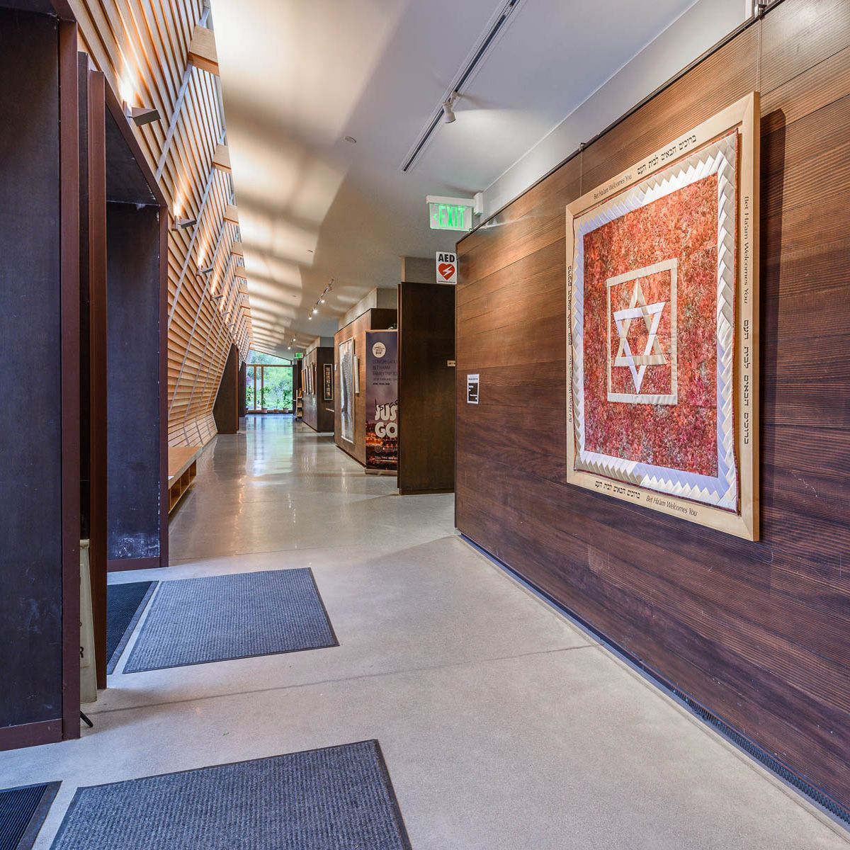 Hallway with wood paneling, artwork, and gray floor mats.