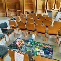 An empty room with rows of wooden chairs, a rug with toys, and wooden walls.