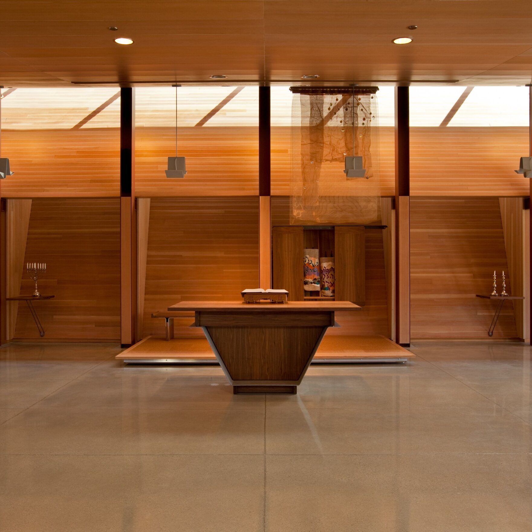 Interior of a chapel with wooden walls, altar, and chandelier, lit by natural light.