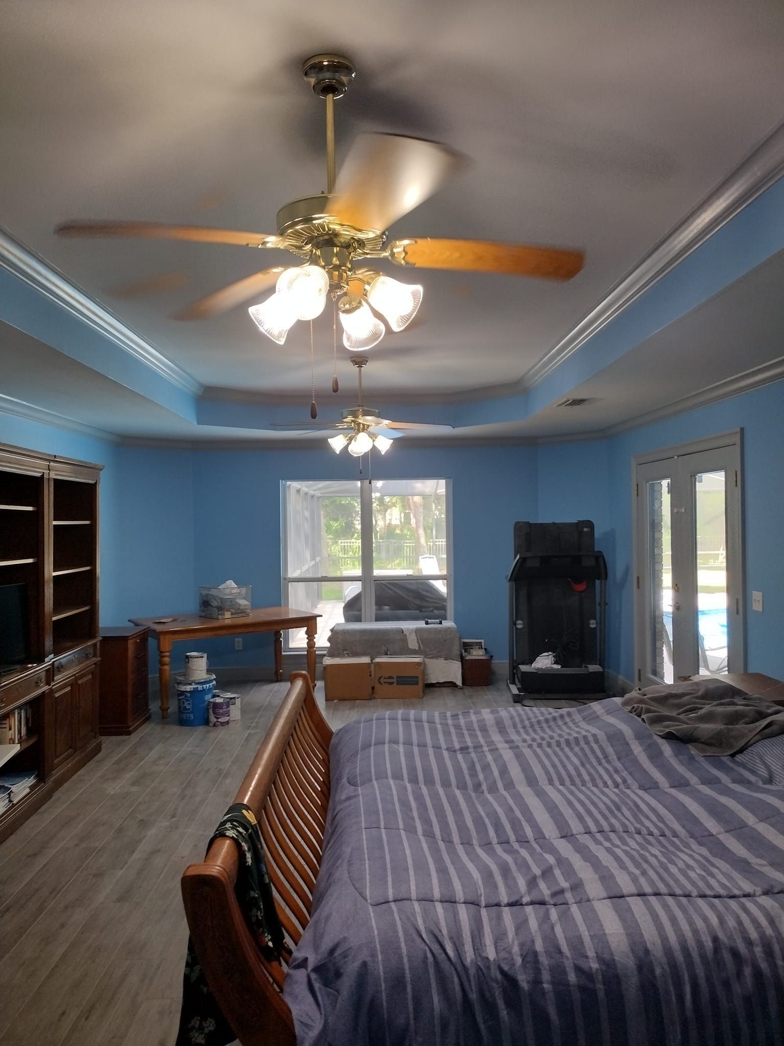 A bedroom with blue walls , a bed , a ceiling fan and a television.
