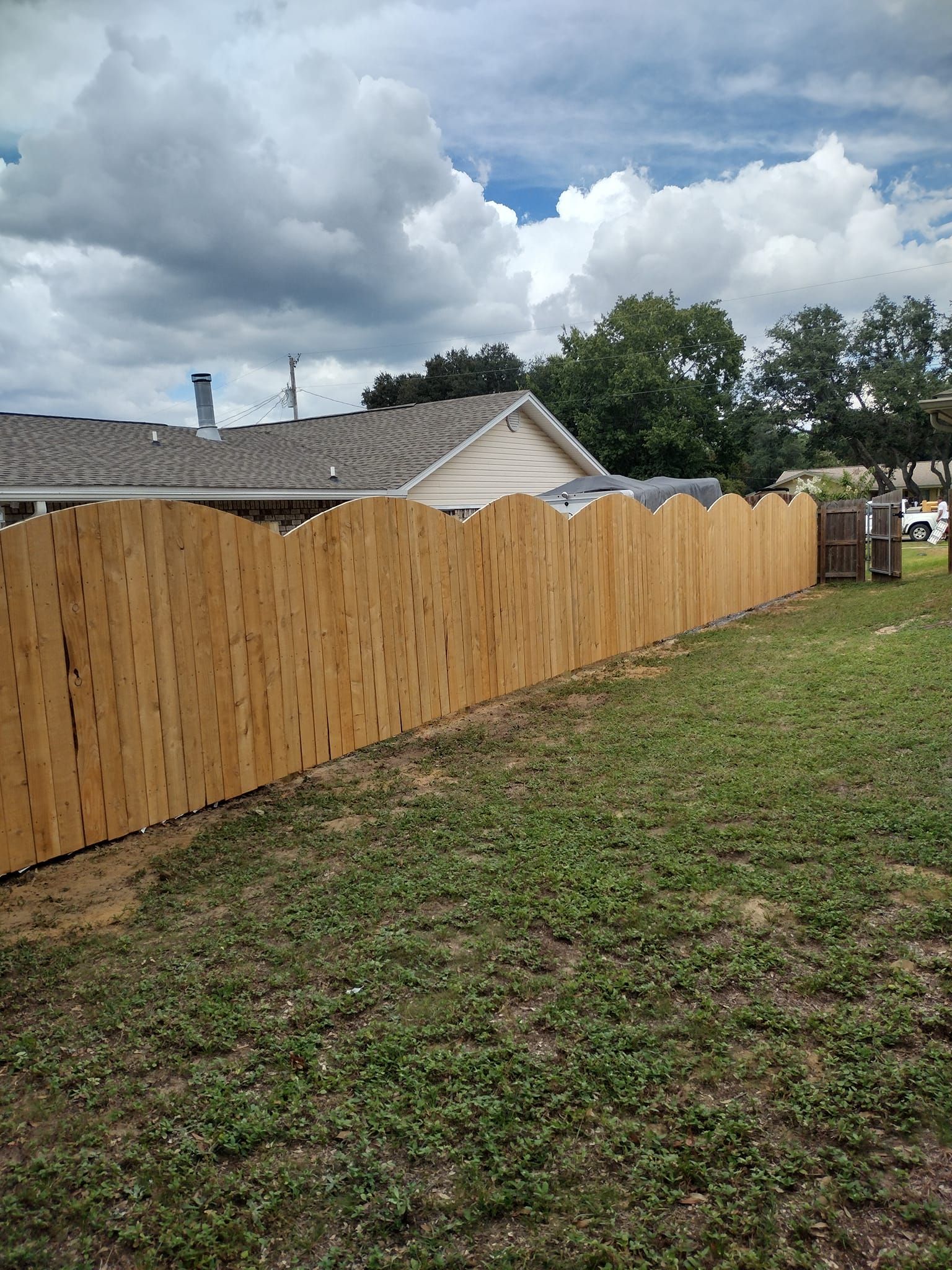 A wooden fence surrounds a grassy yard in front of a house.