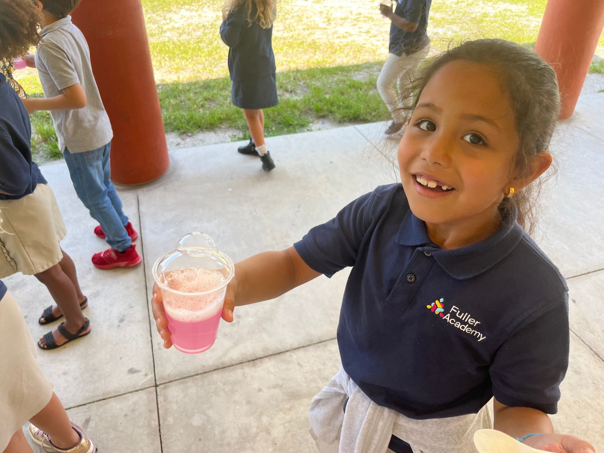 A little girl is holding a cup of pink liquid in her hand.