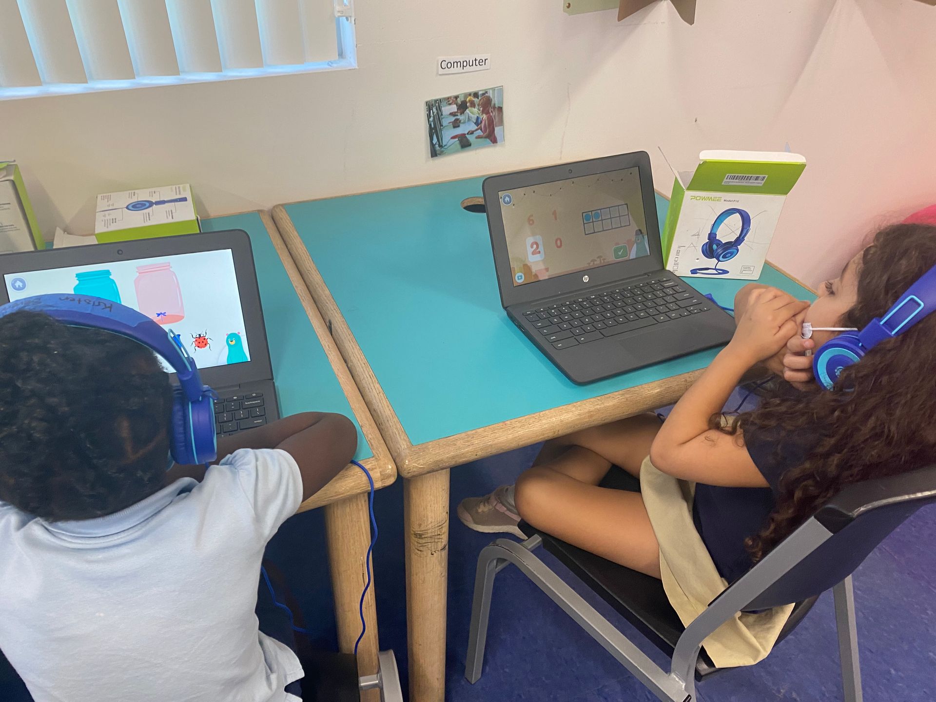 A boy and a girl are sitting at a table with laptops and headphones on.