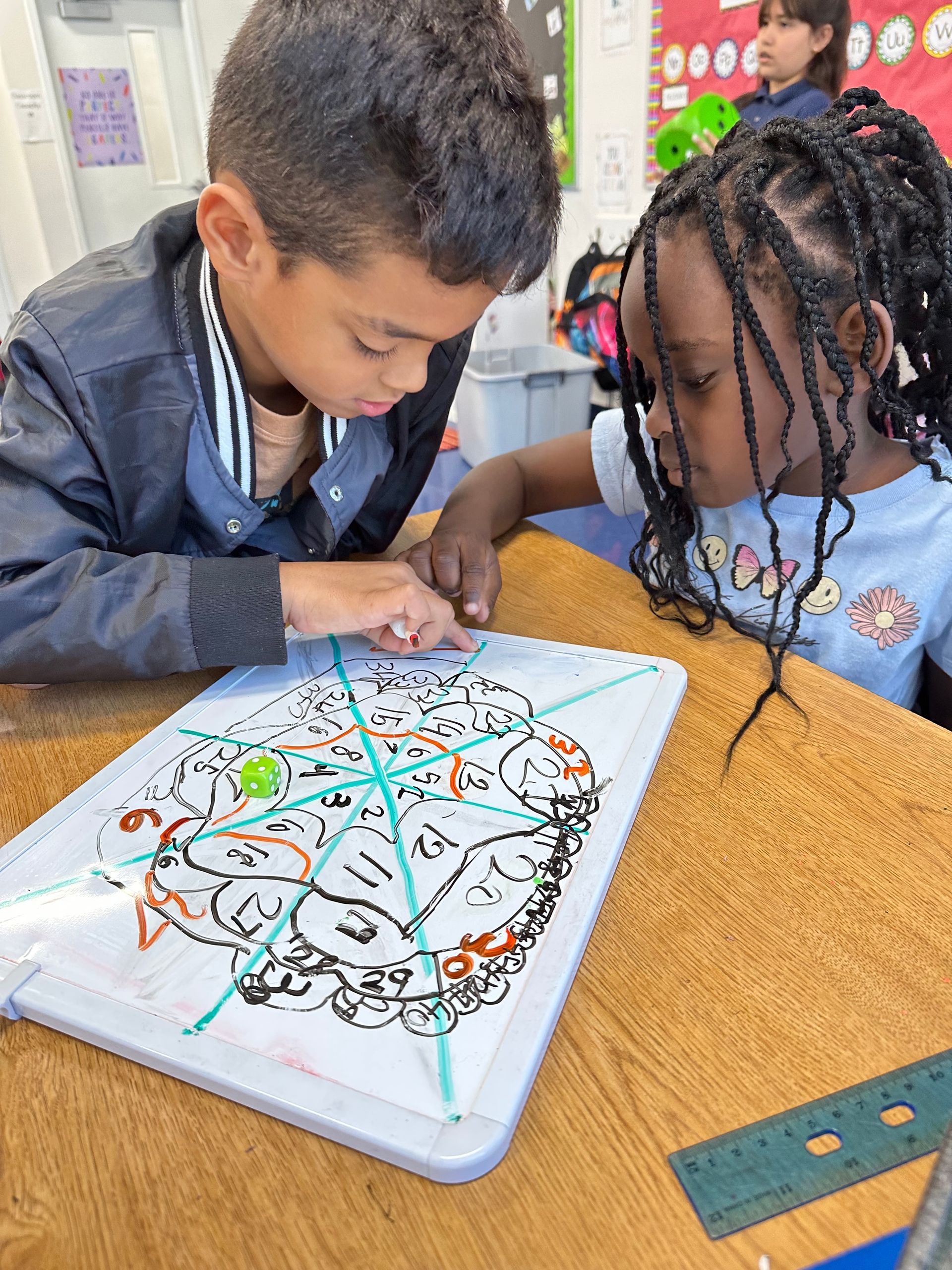 A boy and a girl are sitting at a table drawing on a whiteboard.