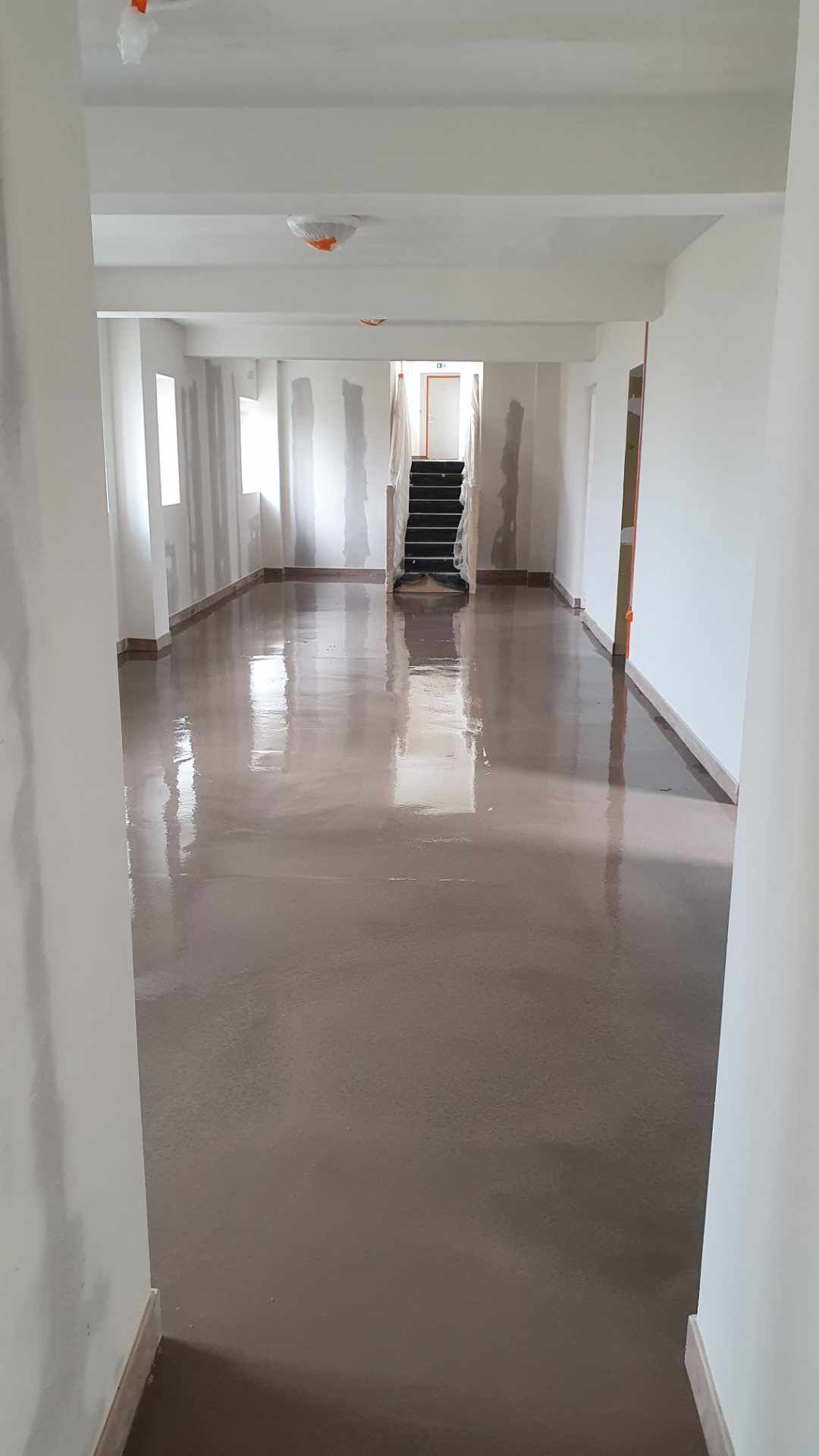 Un long couloir avec un escalier en arrière-plan et un sol brillant avec notre entreprise de peinture normandie.