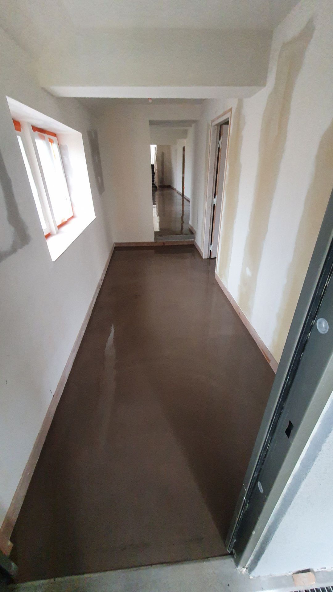 Un long couloir avec un sol marron et des murs blancs avec notre entreprise de peinture normandie.