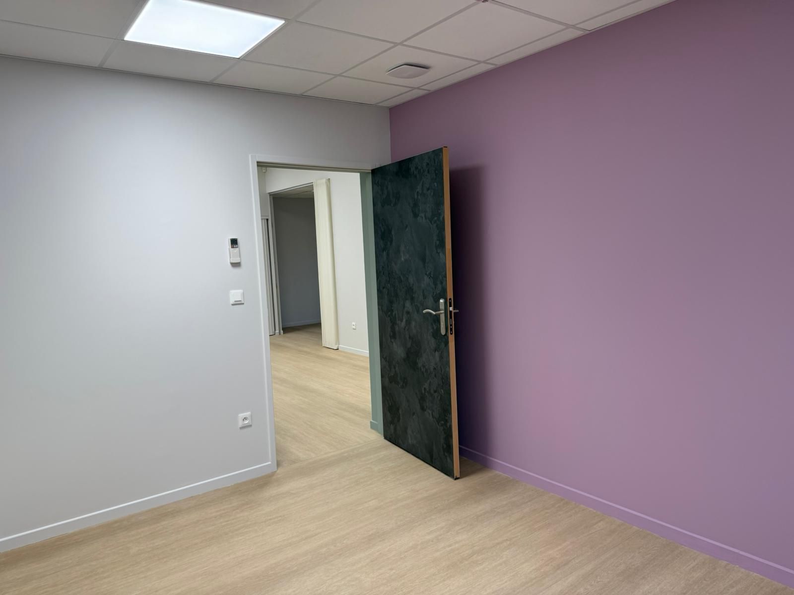 Une pièce vide avec des murs violets et une porte verte avec notre entreprise de peinture normandie.