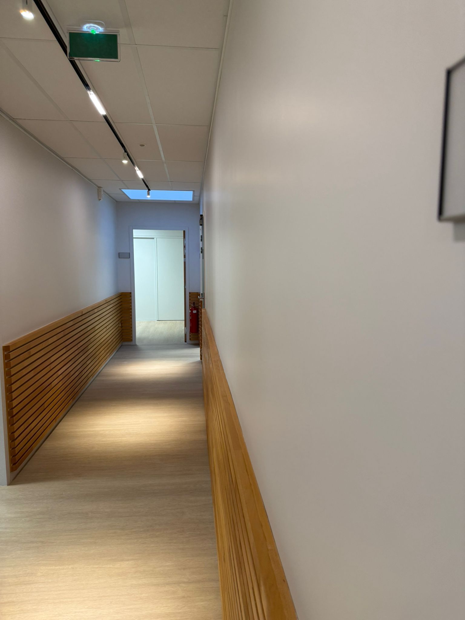 Un long couloir avec une balustrade en bois et des murs blancs menant à une porte avec notre entreprise de peinture