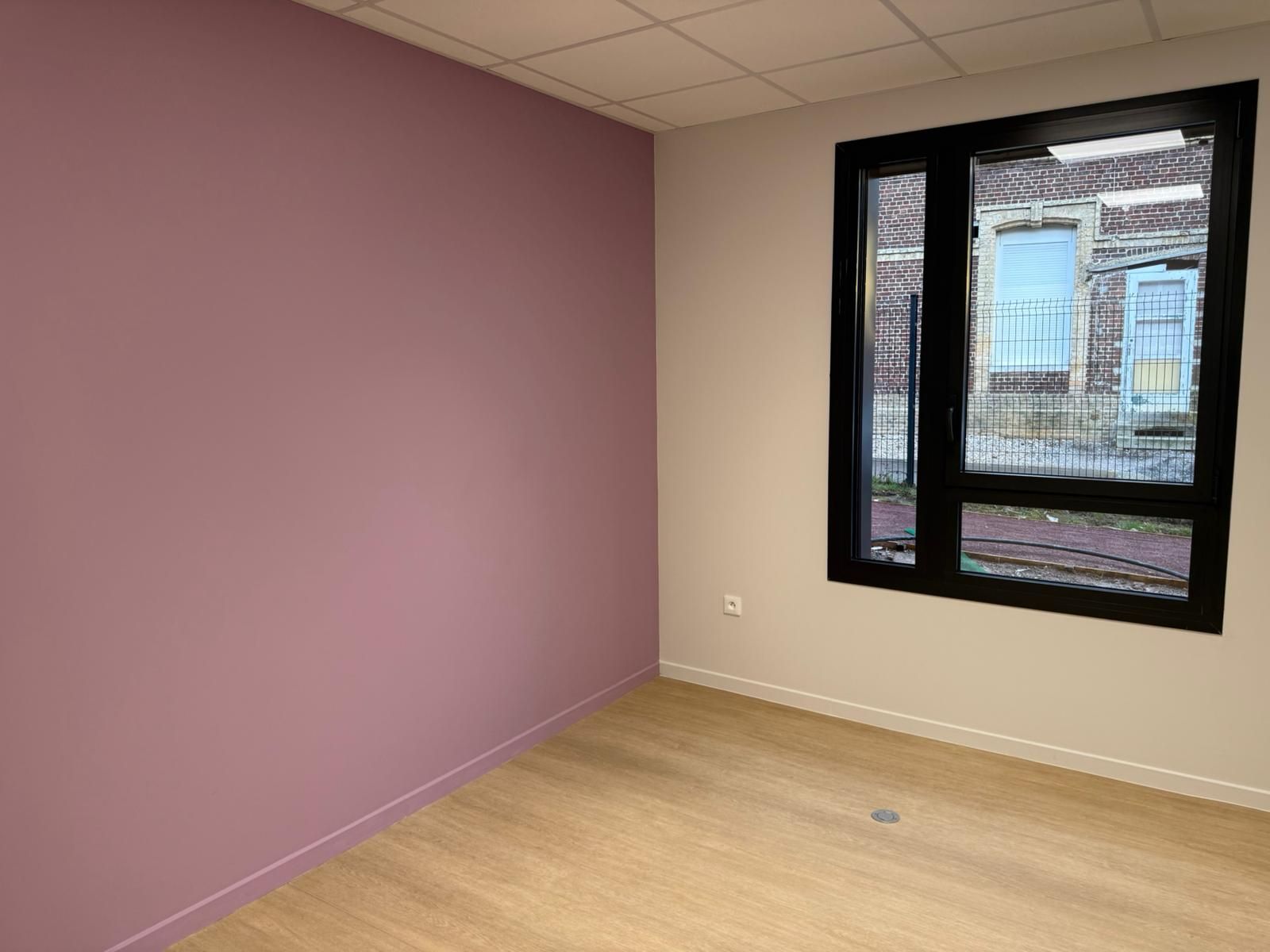 Une pièce vide avec un mur rose et une fenêtre avec notre entreprise de peinture normandie.