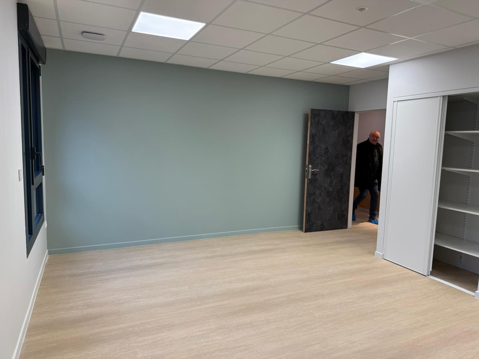 Une pièce vide avec un plancher en bois et un homme debout dans l'embrasure de la porte.