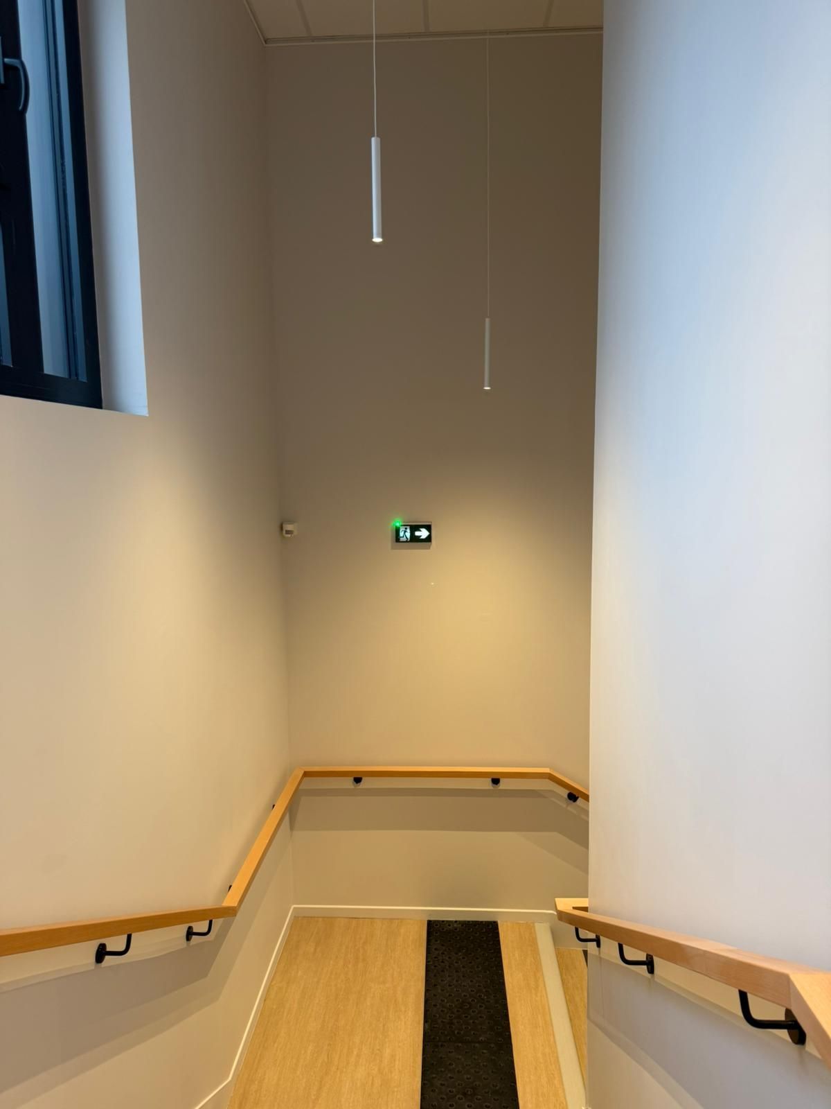 Un escalier avec des rampes en bois et un tapis noir au sol avec notre entreprise de peinture normandie