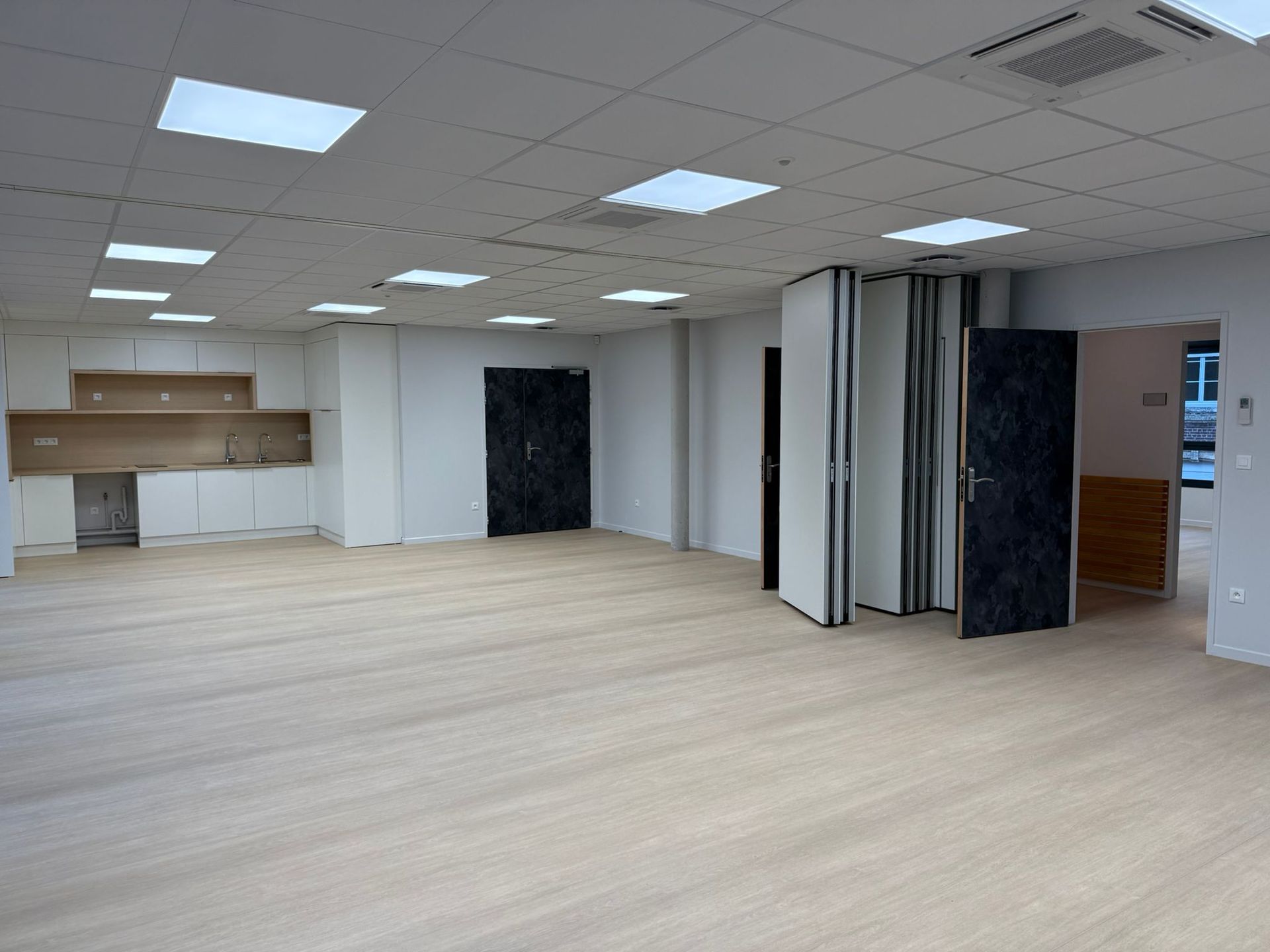 Une grande pièce vide avec du parquet et des murs blancs avec notre entreprise de peinture normandie