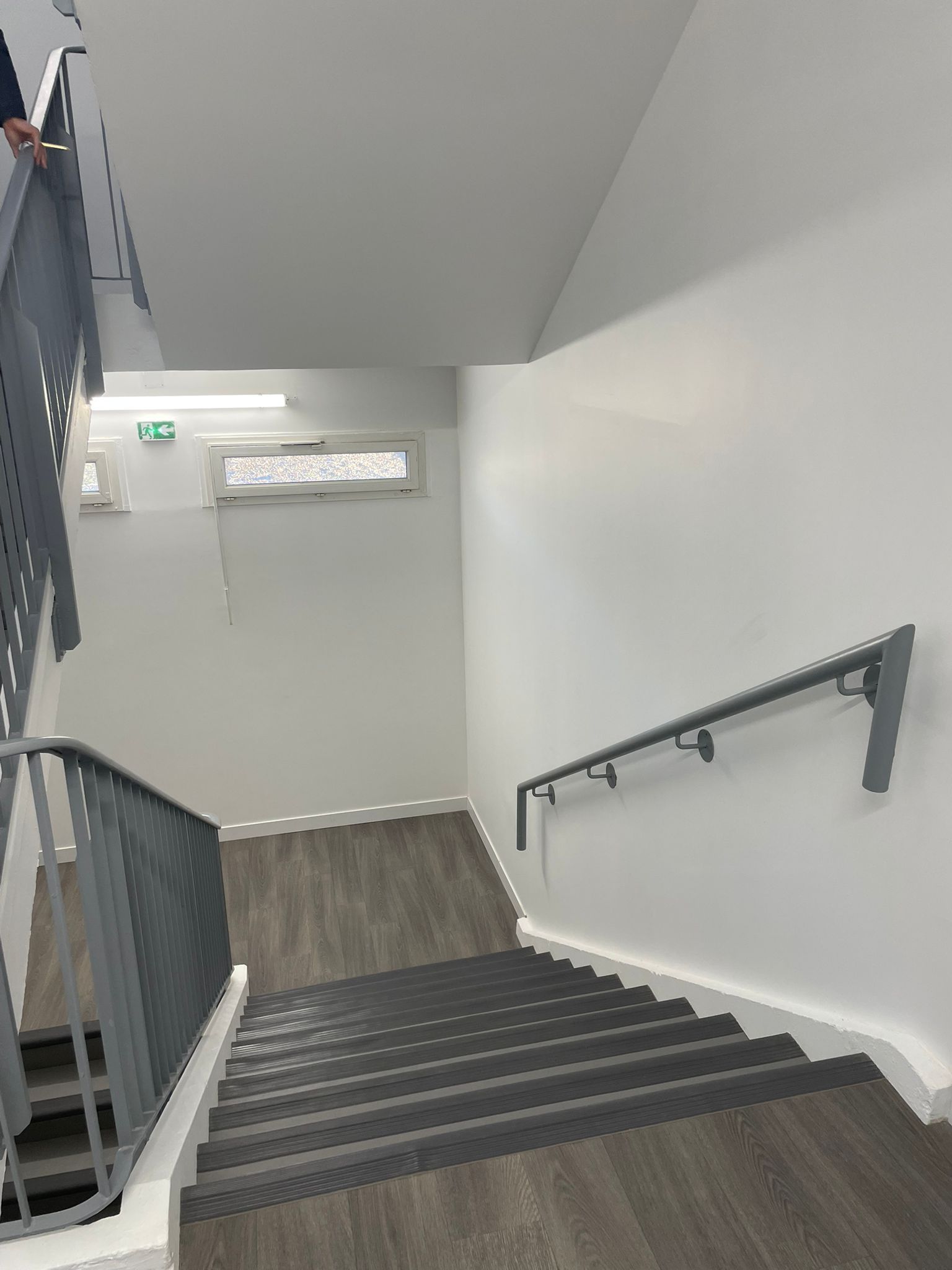 Un escalier avec une rampe en métal et un plancher en bois dans un bâtiment avec notre entreprise de peinture normandie.