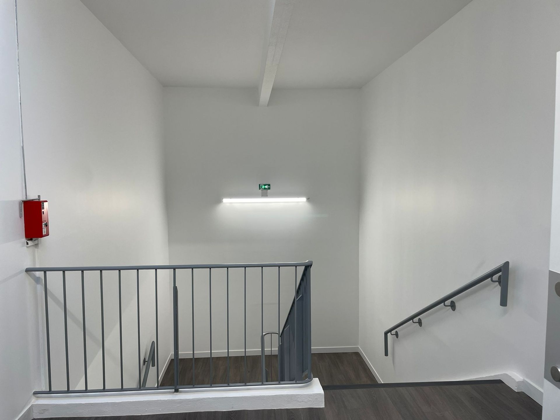 Un escalier avec une rampe et un extincteur au mur avec notre entreprise de peinture normandie.