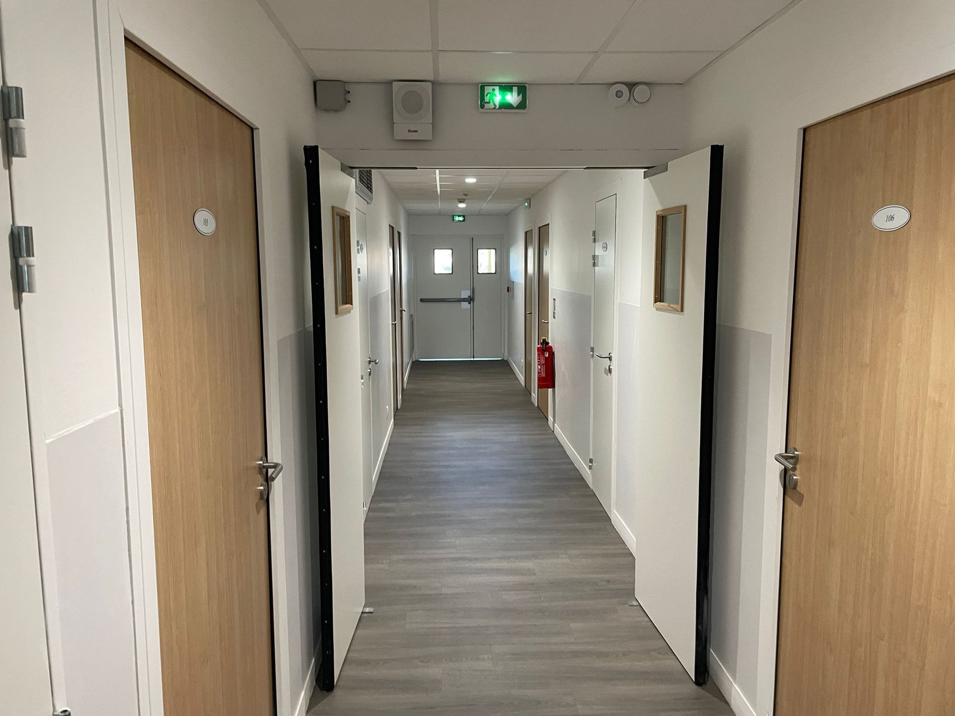 Un long couloir avec des portes en bois dans un bâtiment avec notre entreprise de peinture normandie
