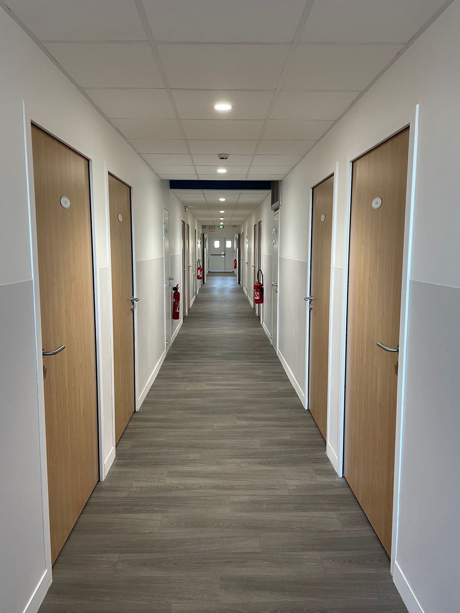Un long couloir avec des portes en bois dans un bâtiment avec notre entreprise de peinture normandie