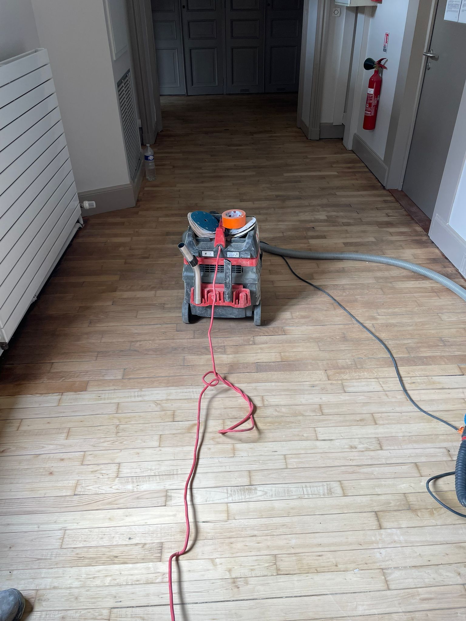 Un aspirateur est posé sur un plancher en bois dans un couloir avec notre entreprise de peinture normandie.