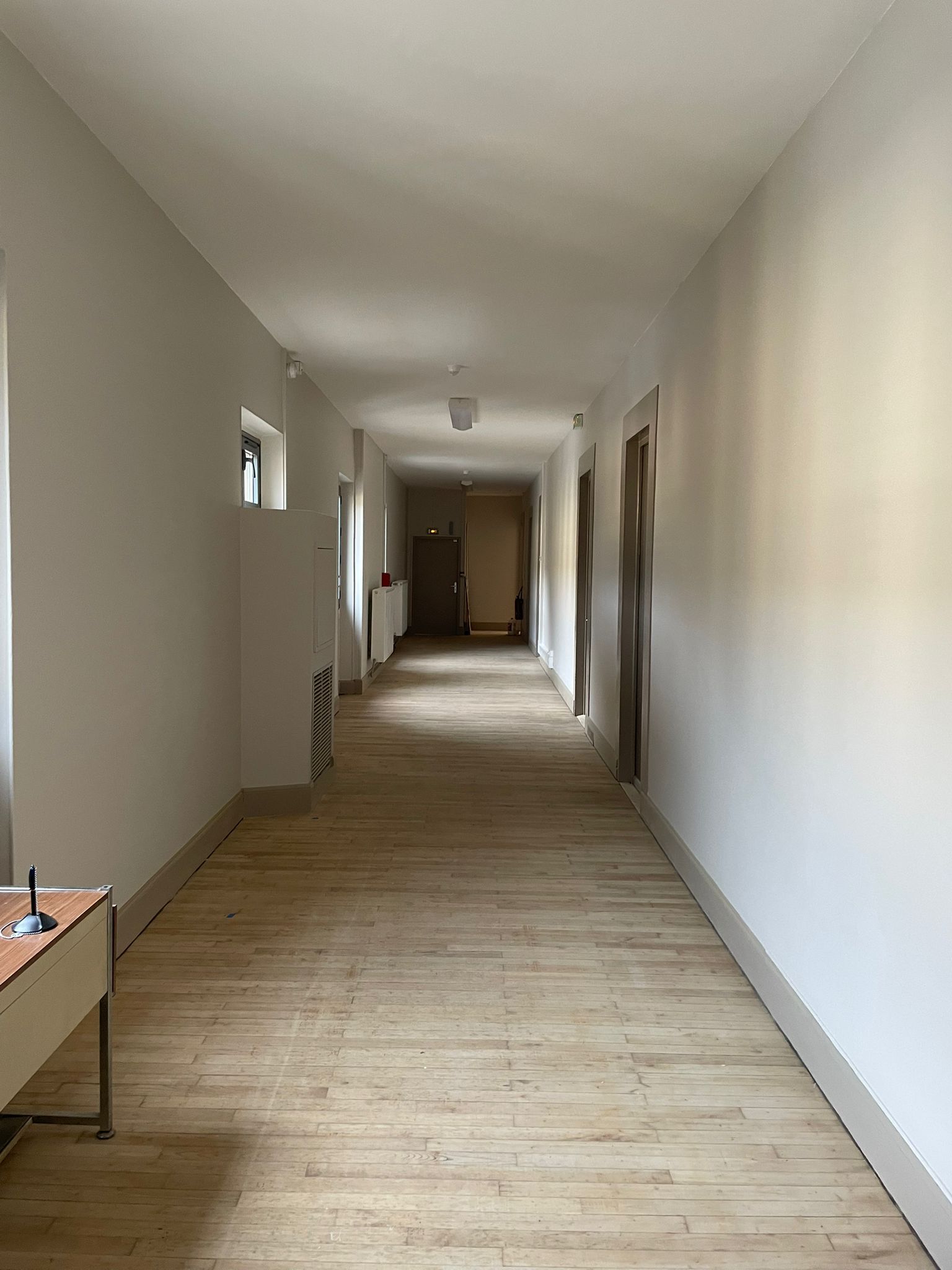 Un long couloir avec du parquet et des murs blancs avec notre entreprise de peinture normandie.